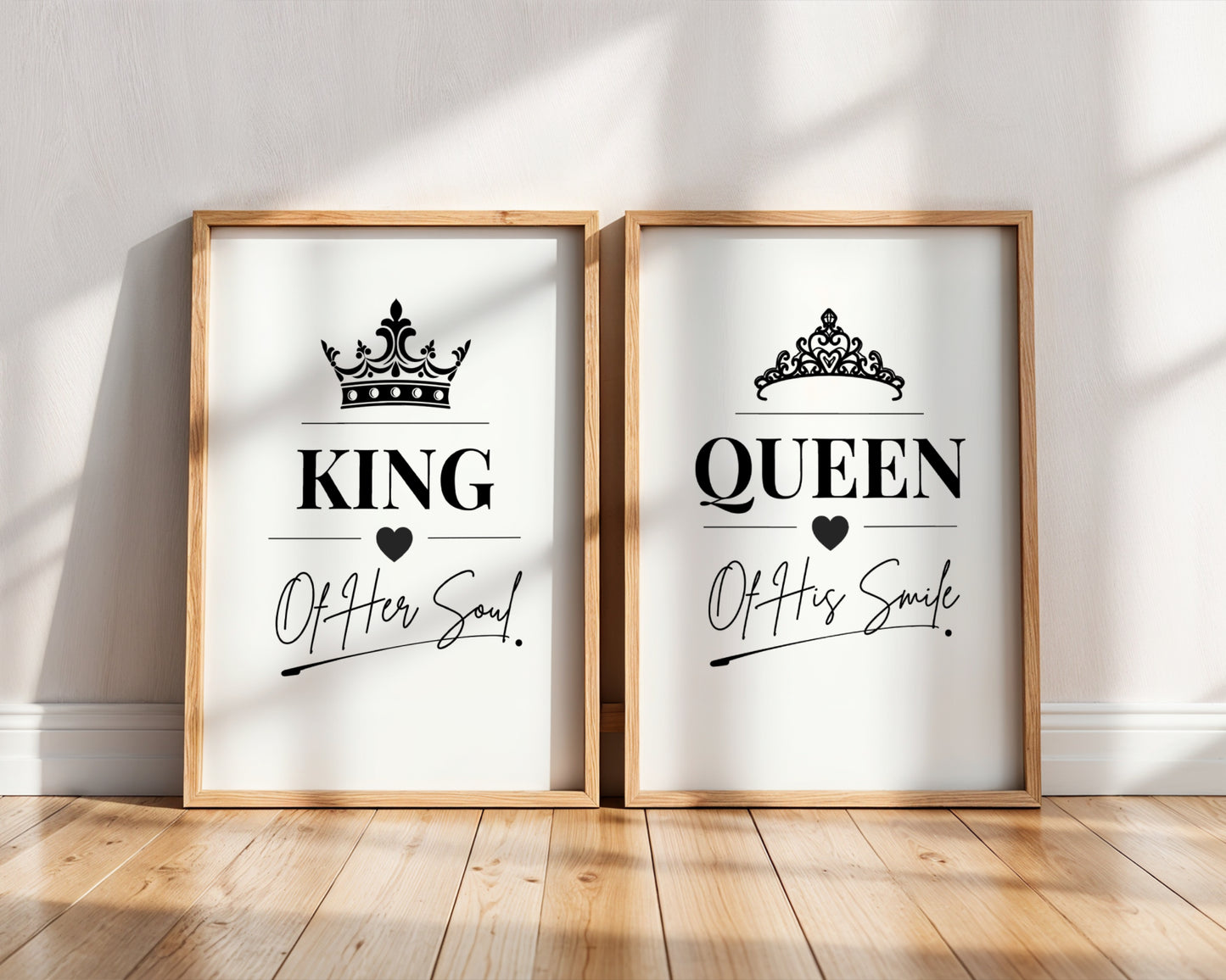 Two framed wall art prints leaning against a white wall on a wood floor. The left print says KING with a crown and 'Of Her Soul!' and the right print says QUEEN with a crown and 'Of His Smile!'.