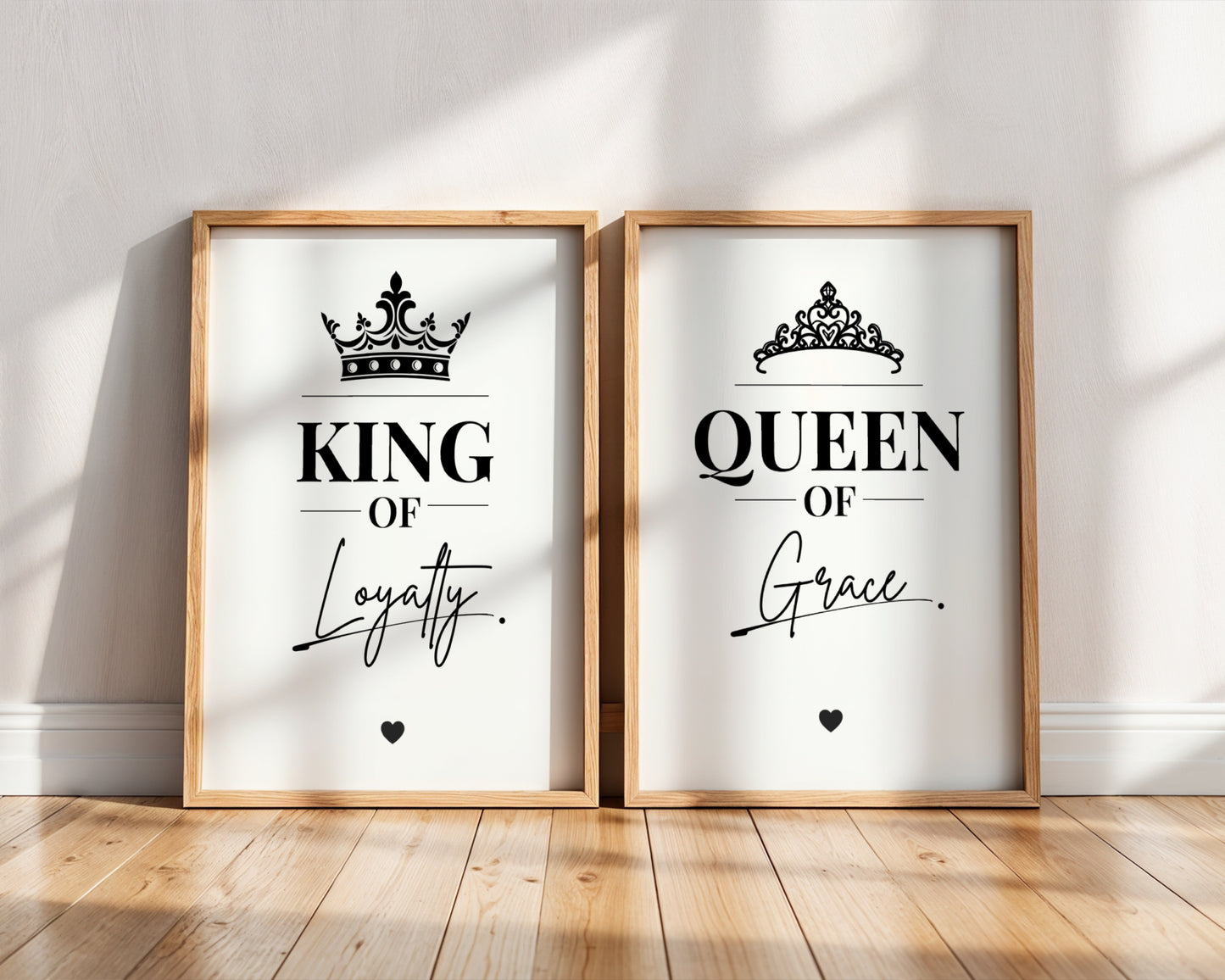 Two framed wall art prints leaning against a white wall on a wood floor. The left print says "KING OF Loyalty" with a black crown above, and the right print says "QUEEN OF Grace" with a black tiara above.