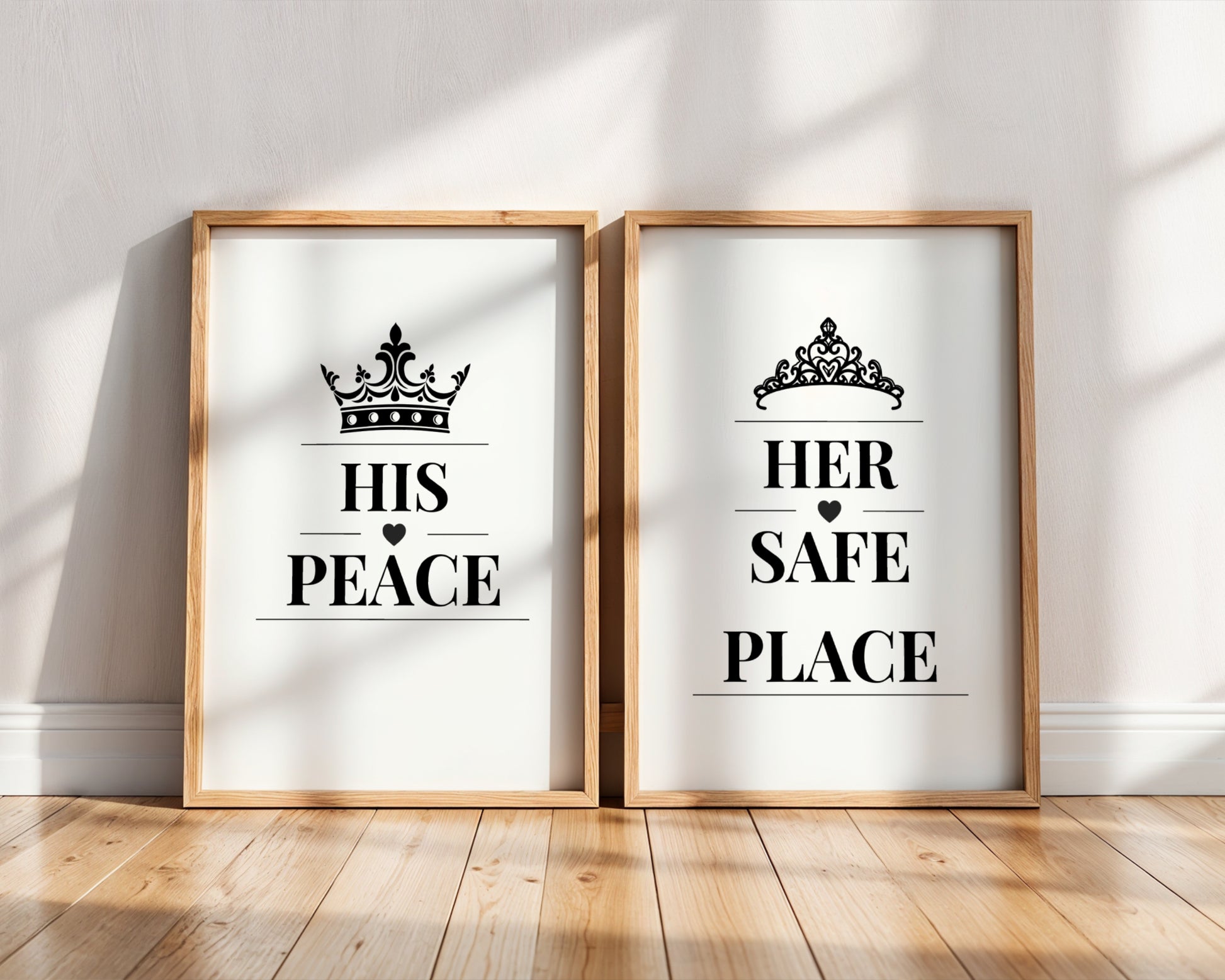 Two framed black-and-white typographic wall art prints leaning against a white wall on a wood floor. The left print says "HIS PEACE" with a crown above, and the right print says "HER SAFE PLACE" with a tiara above.