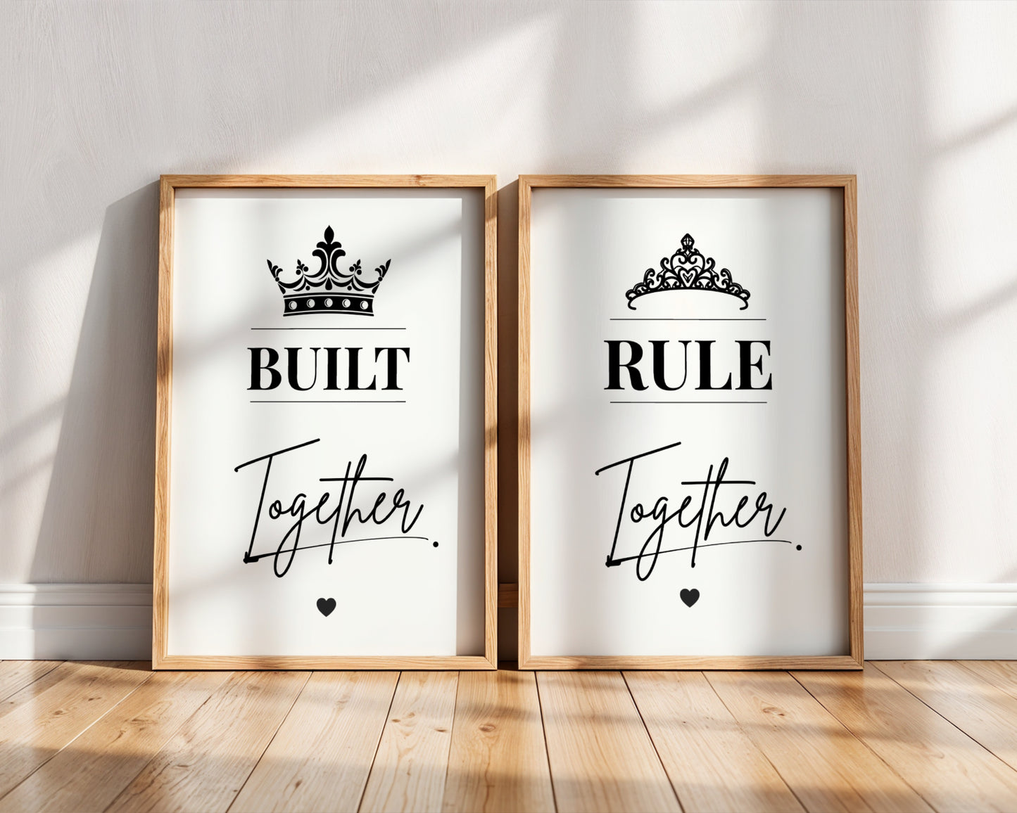 Two framed wall art prints leaning against a white wall on a wood floor. The left print says 'BUILT Together' with a black crown above, and the right print says 'RULE Together' with a black tiara above.