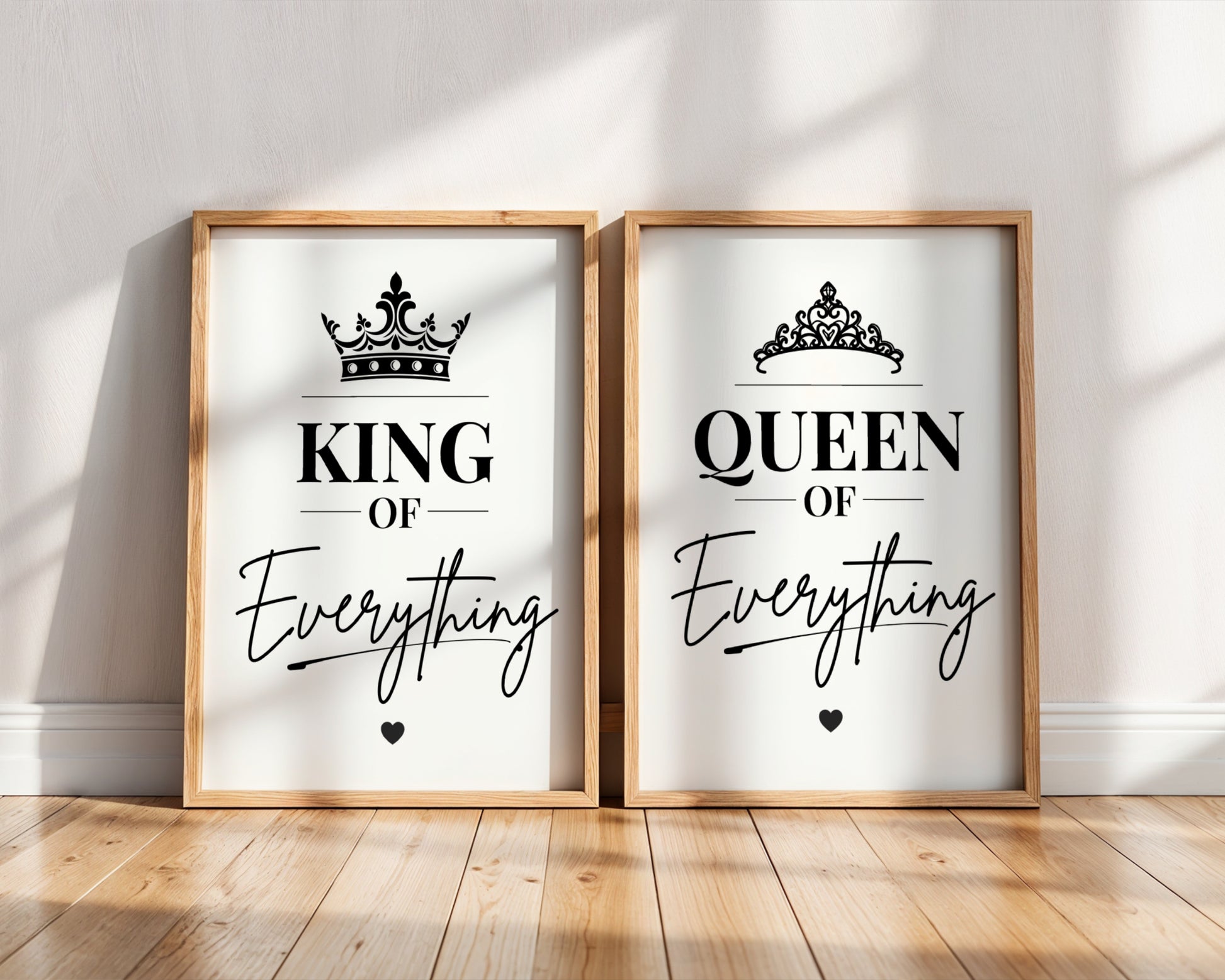 Two framed wall art prints leaning against a white wall on a wood floor. The left print says "KING OF Everything" with a black crown graphic, and the right print says "QUEEN OF Everything" with a black tiara graphic.