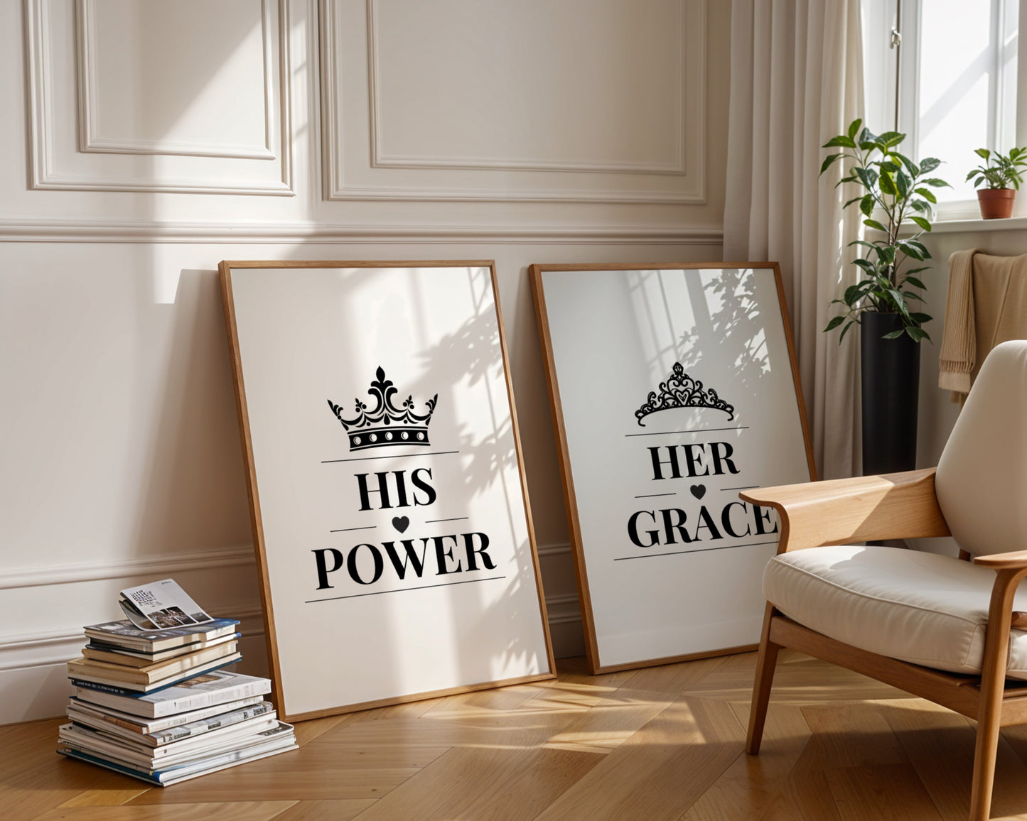 Two framed art prints leaning against a cream paneled wall on a wooden floor, styled in a bright living room next to a wooden armchair and potted plants. The left print reads 'HIS POWER' with a crown graphic, and the right print reads 'HER GRACE' with a tiara graphic.