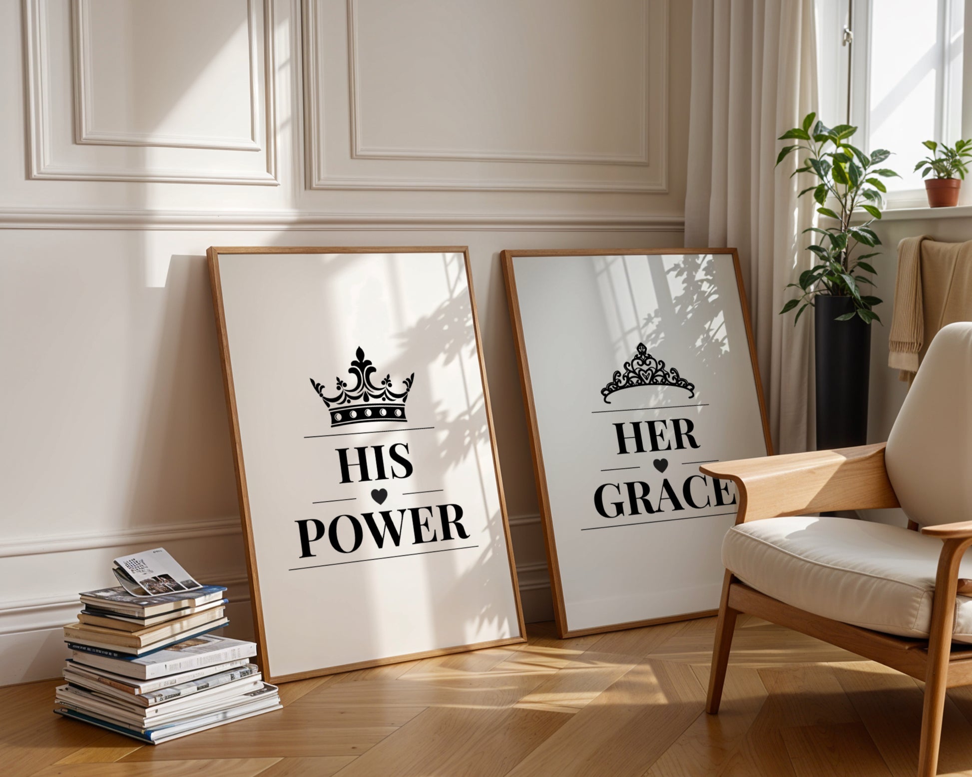 Two framed art prints leaning against a cream paneled wall on a wooden floor, styled in a bright living room next to a wooden armchair and potted plants. The left print reads 'HIS POWER' with a crown graphic, and the right print reads 'HER GRACE' with a tiara graphic.