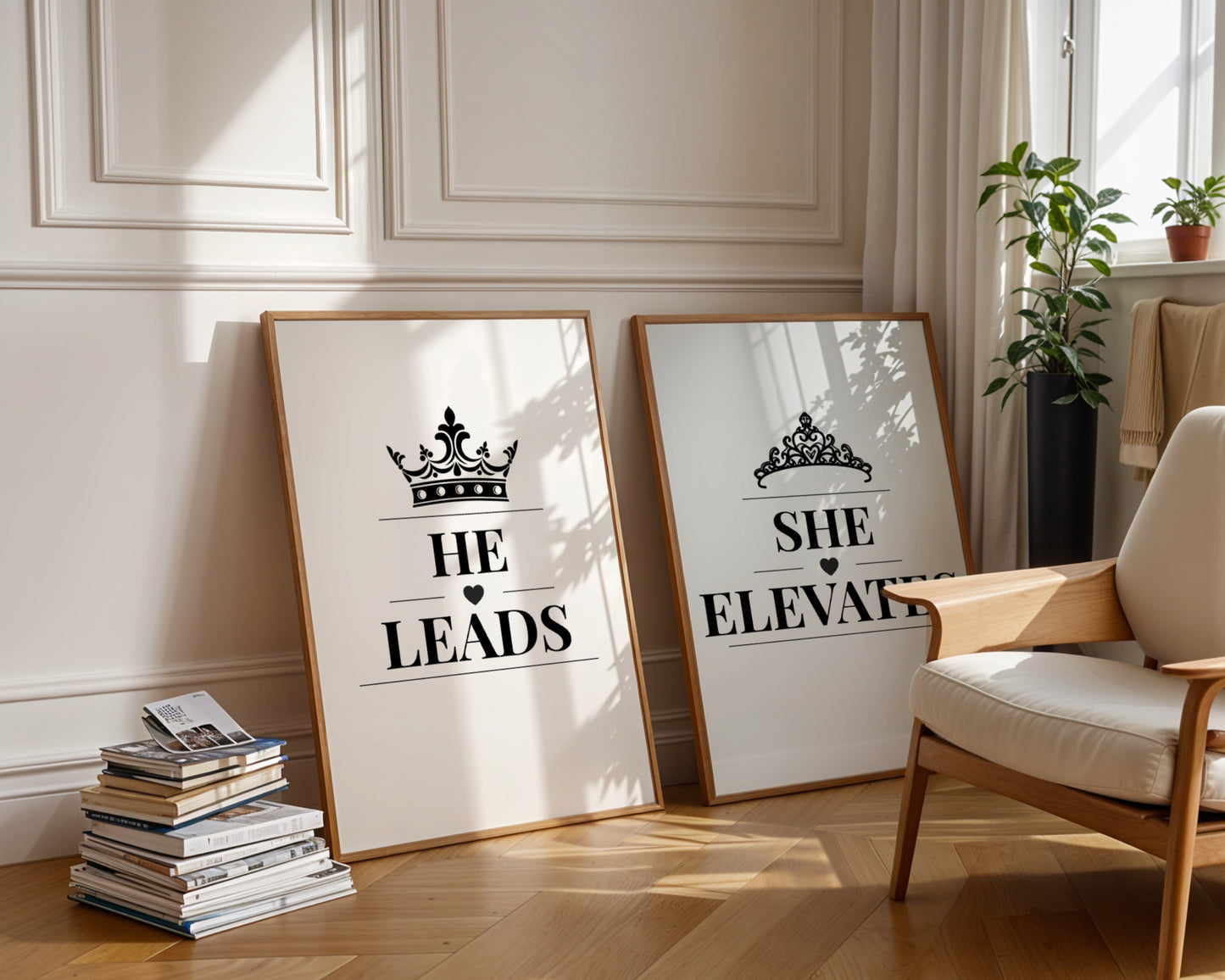 Two framed motivational art prints leaning against a cream paneled wall in a sunlit room. The left print says 'HE LEADS' with a crown graphic, and the right print says 'SHE ELEVATES' with a tiara graphic.