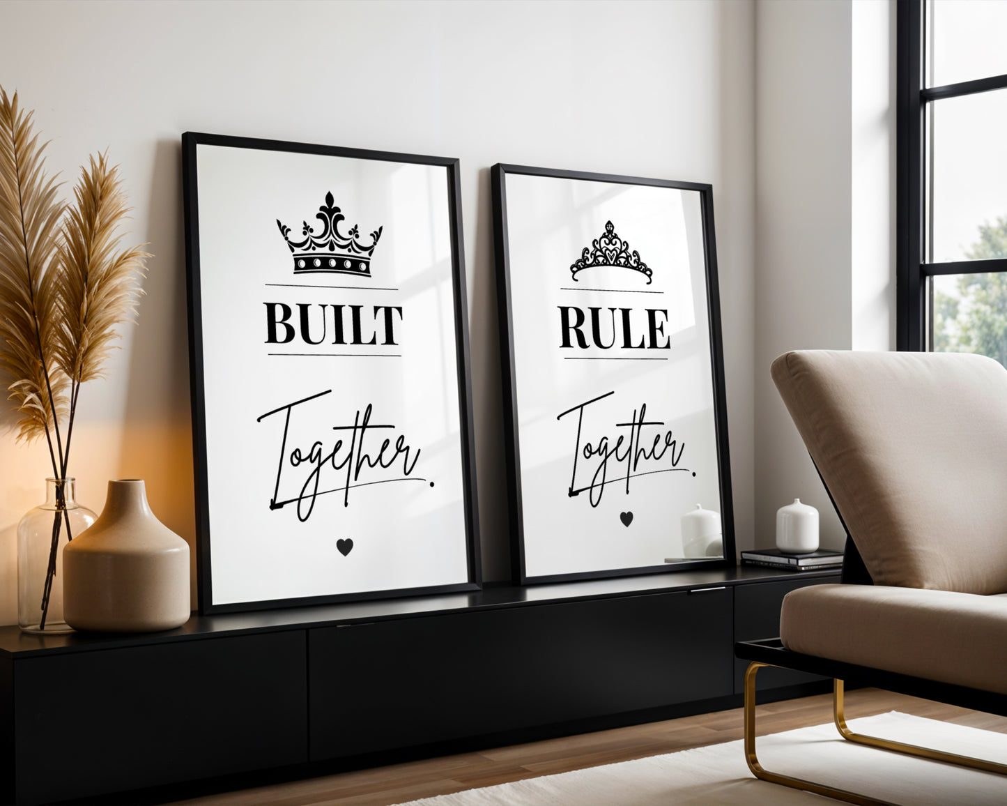 Two framed black-and-white typography wall art prints leaning against a wall in a modern living room. The left print reads 'BUILT Together' with a crown above, and the right print reads 'RULE Together' with a tiara above.