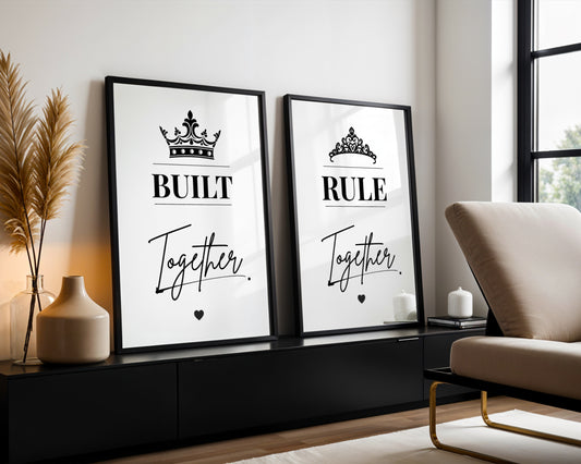 Two framed black-and-white typography wall art prints leaning against a wall in a modern living room. The left print reads 'BUILT Together' with a crown above, and the right print reads 'RULE Together' with a tiara above.