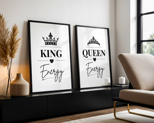 Two framed black-and-white decorative prints leaning against a wall in a modern living room. The left print says KING Energy with a crown above, and the right print says QUEEN Energy with a tiara above.