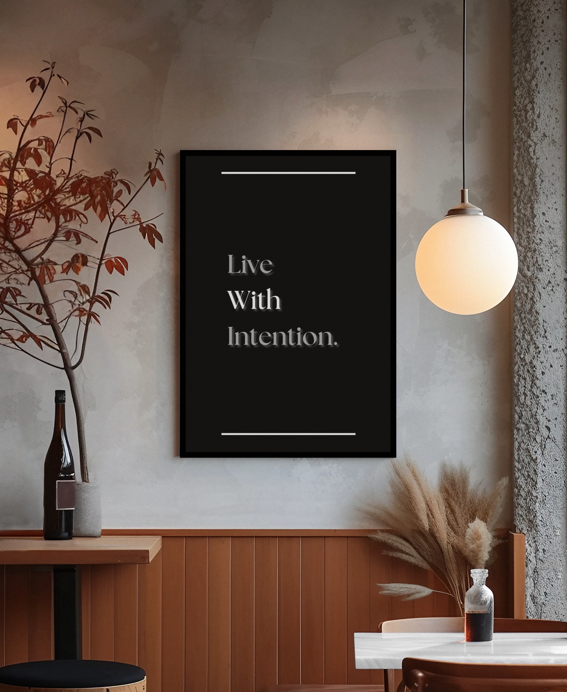 A black framed wall art print with the text 'Live With Intention.' in white serif lettering, displayed in a warm, modern interior setting with a hanging globe lamp, wood-paneled wall, and decorative dried grasses.