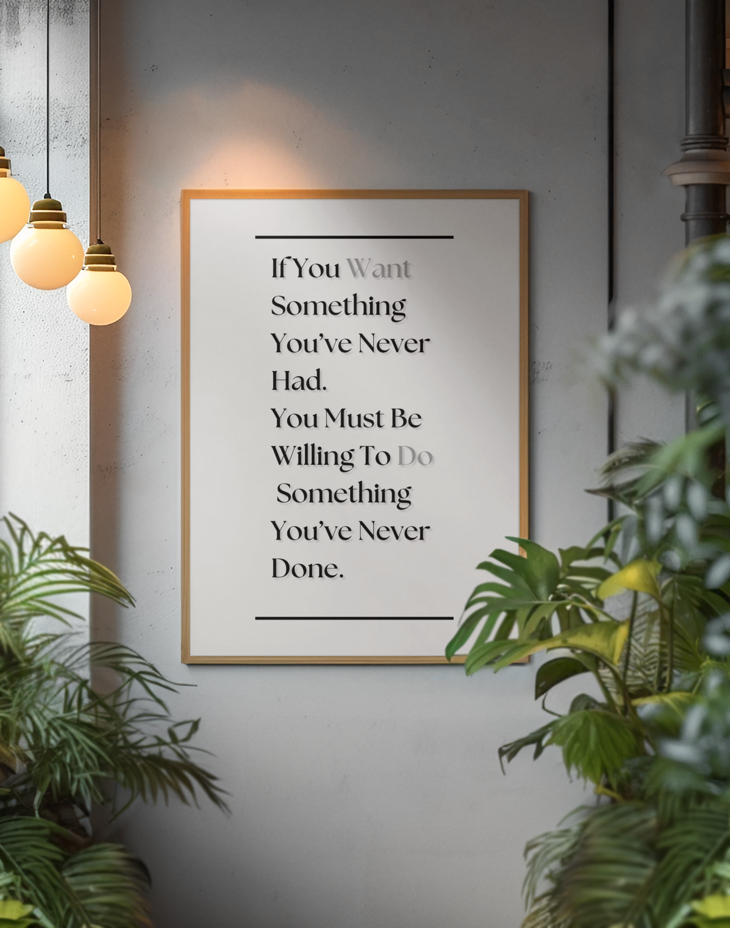 A framed motivational wall art print with the text 'If You Want Something You've Never Had. You Must Be Willing To Do Something You've Never Done.' in white serif lettering on a black background, hanging on a gray wall in a styled interior with hanging pendant lights and green plants.
