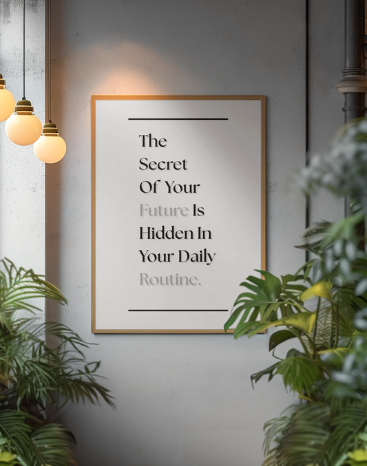 A framed motivational quote print hanging on a gray wall, surrounded by green plants and warm hanging pendant lights. The print reads, 'The Secret Of Your Future Is Hidden In Your Daily Routine'.
