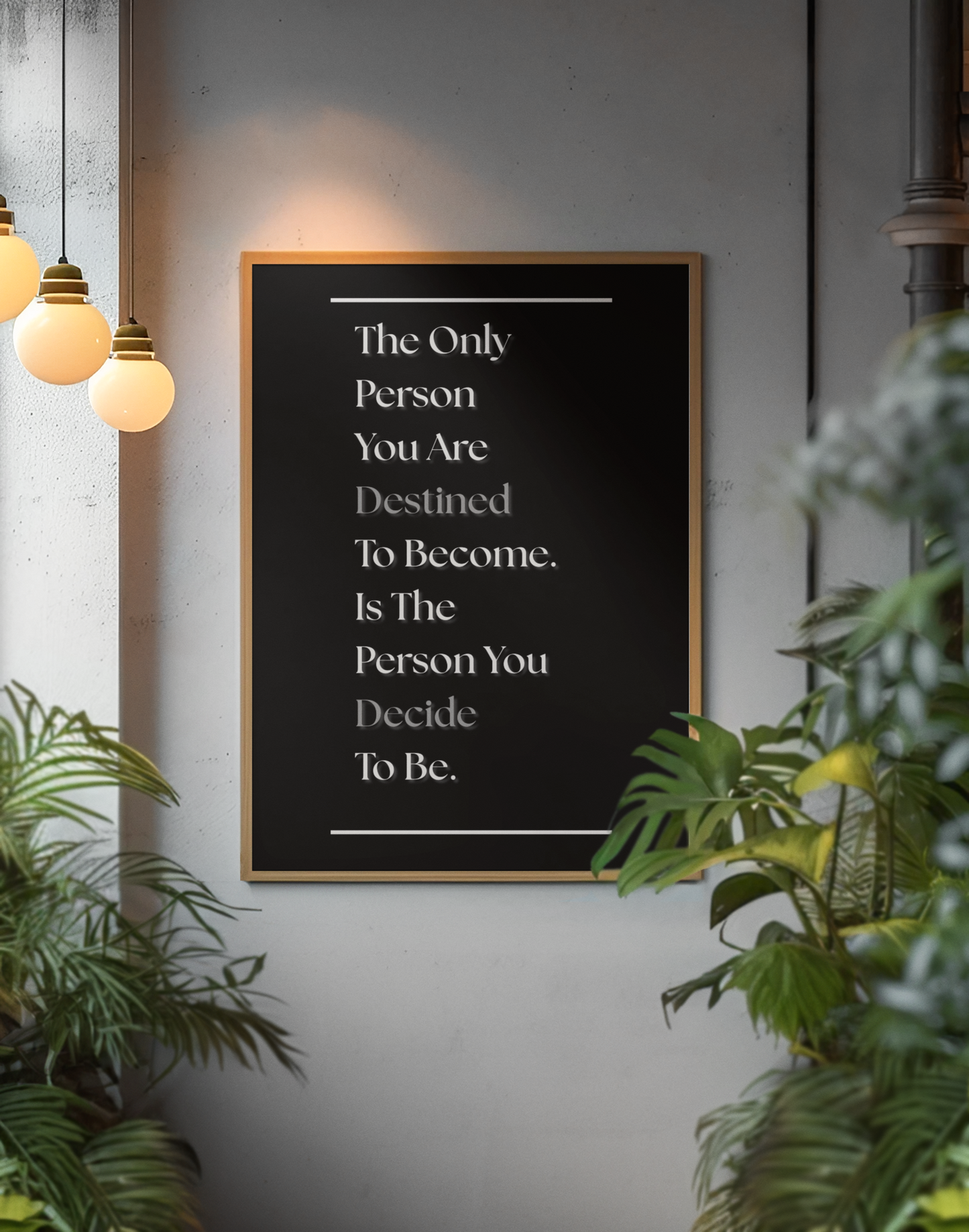 A framed typographic wall art print with a motivational quote in white text on a black background, hanging on a gray wall in a styled interior with hanging pendant lights and green plants.