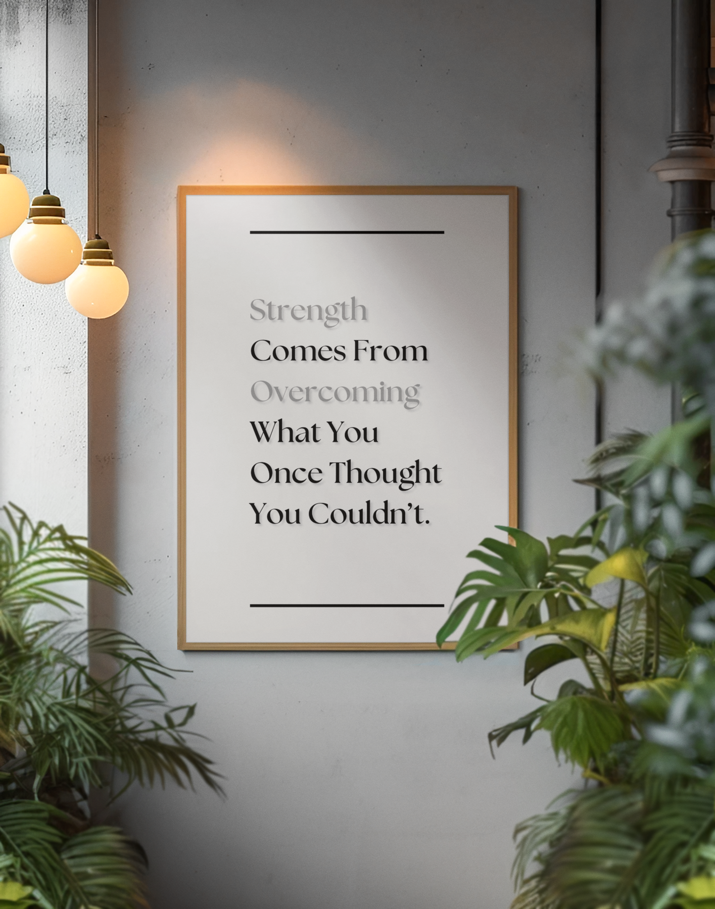 A framed motivational wall art print with the quote 'Strength Comes From Overcoming What You Once Thought You Couldn't.' displayed on a gray wall, surrounded by green plants and warm hanging pendant lights.