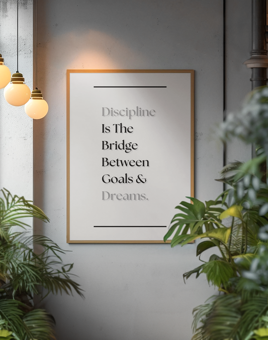 A framed motivational wall art print with the quote 'Discipline Is The Bridge Between Goals & Dreams.' displayed on a gray wall, surrounded by green plants and warm hanging pendant lights.