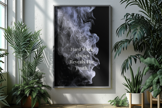 A framed vertical wall art print hangs on a light wall in a styled interior. The print shows a black background with white smoke and the text 'Hard Work Always Reveals The Truth'.