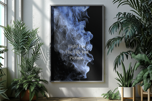 A framed vertical wall art print hangs on a light wall in a styled interior. The artwork shows a black background with blue-white smoke and the text 'Fight For The Life You Picture'.
