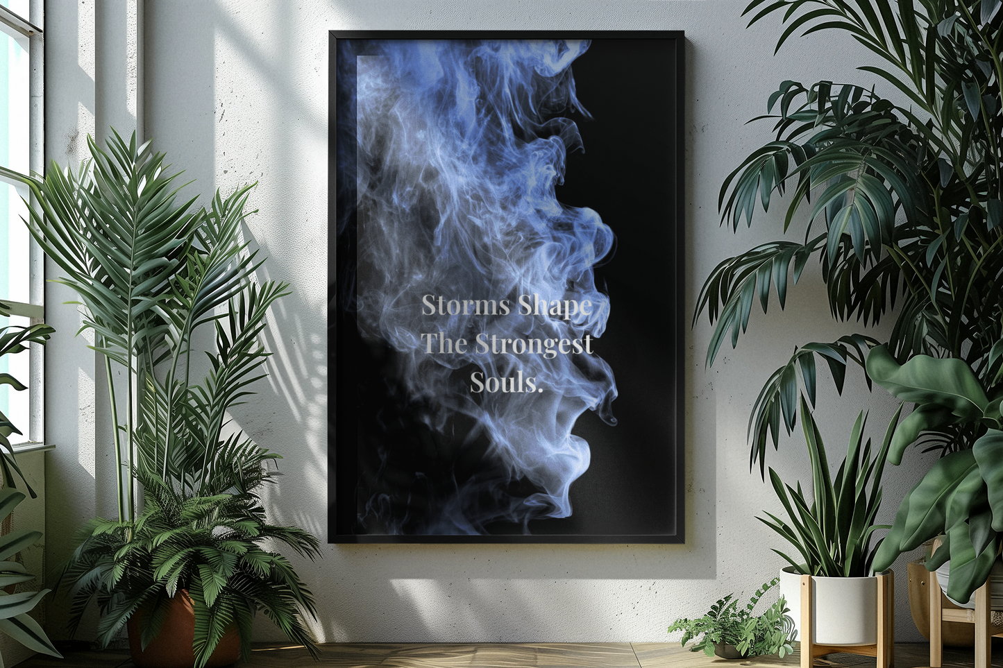 A framed vertical wall art print hanging on a white wall in a bright room with potted plants. The print features a black background with a blue and white smoke-like graphic and the text 'Storms Shape The Strongest Souls.
