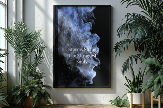 A framed vertical wall art print hanging on a white wall in a bright room with potted plants. The print features a black background with a blue and white smoke-like graphic and the text 'Storms Shape The Strongest Souls.