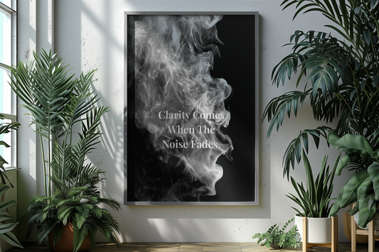 A framed vertical wall art print hanging on a light gray wall, featuring a black-and-white smoke graphic with the text 'Clarity Comes When The Noise Fades'. The room is styled with potted green plants on both sides.