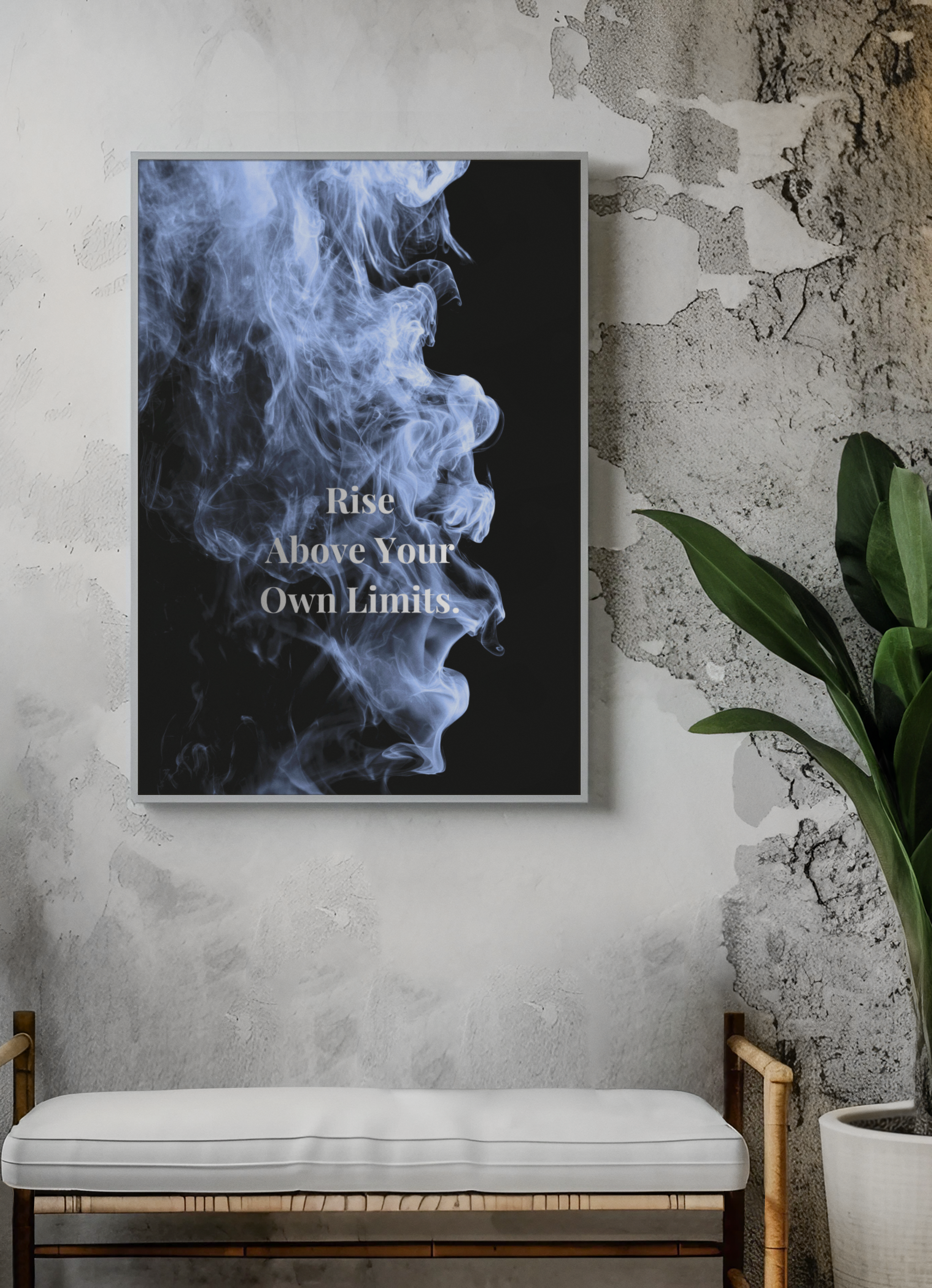 A framed wall art print featuring a black background with blue-white smoke and the text 'Rise Above Your Own Limits', displayed on a textured gray wall above a white cushioned bench, with a green potted plant to the right.