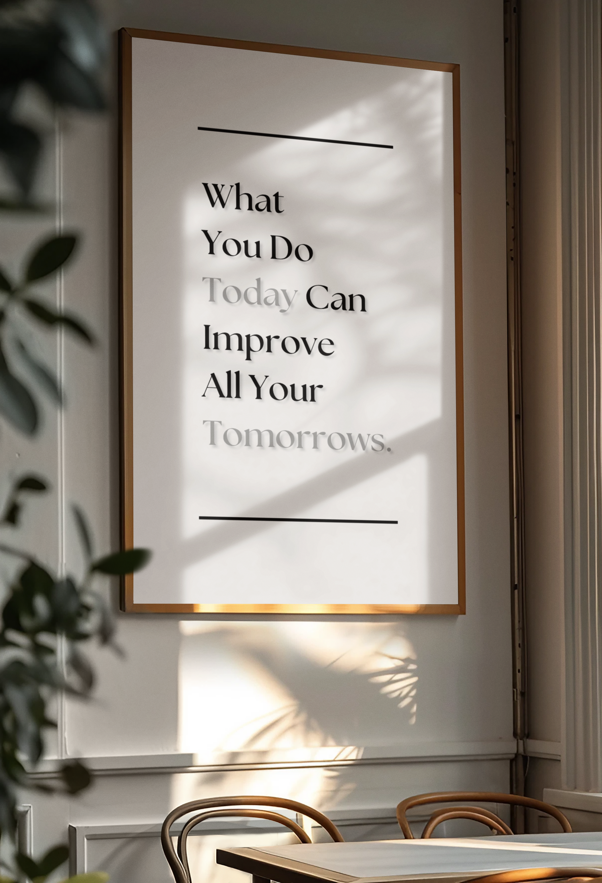 A framed motivational wall art print hanging on a light gray wall in a dining room. The print features a warm gold frame, a white background, and black text that reads, 'What You Do Today Can Improve All Your Tomorrows.'