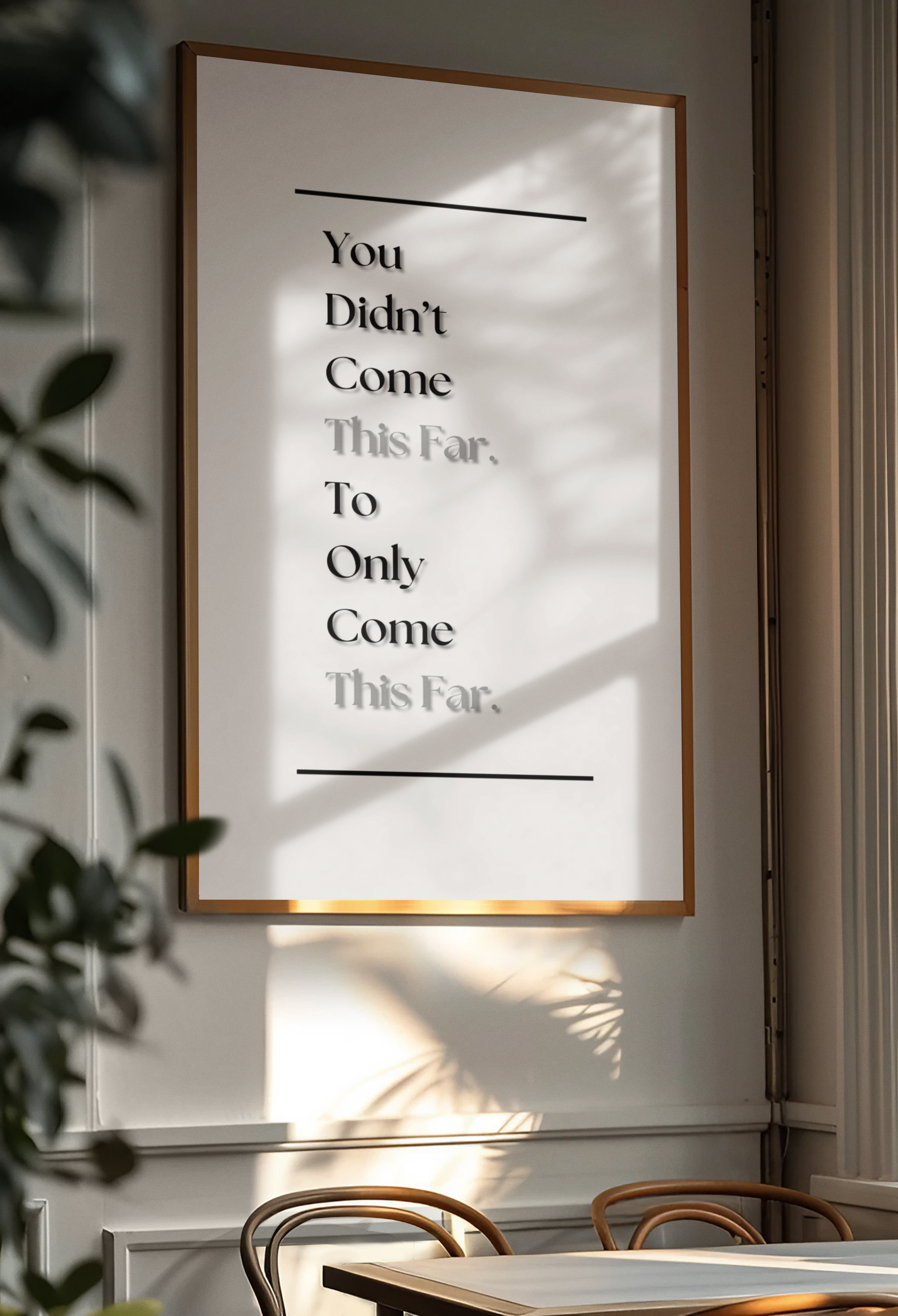 A framed typographic wall art print hanging on a light wall in a real interior setting, with sunlight and leaf shadows cast across it. The print contains only black text on a white background: 'You Didn't Come This Far, To Only Come This Far'.