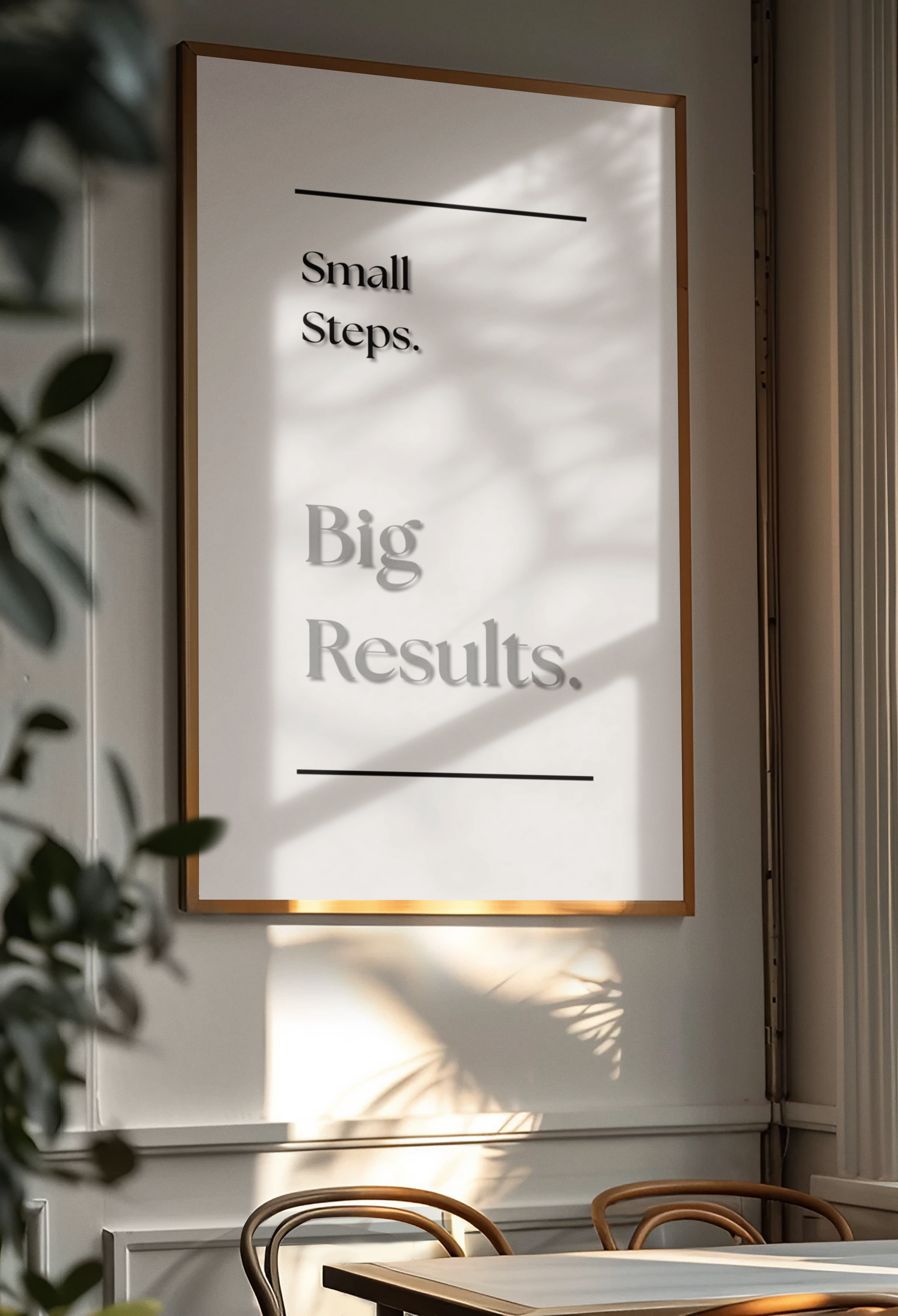 A framed motivational wall art print with the text 'Small Steps. Big Results.' in black serif font on a white background, hanging on a light wall in a real interior setting with sunlight, shadows, and part of a table and chairs visible.
