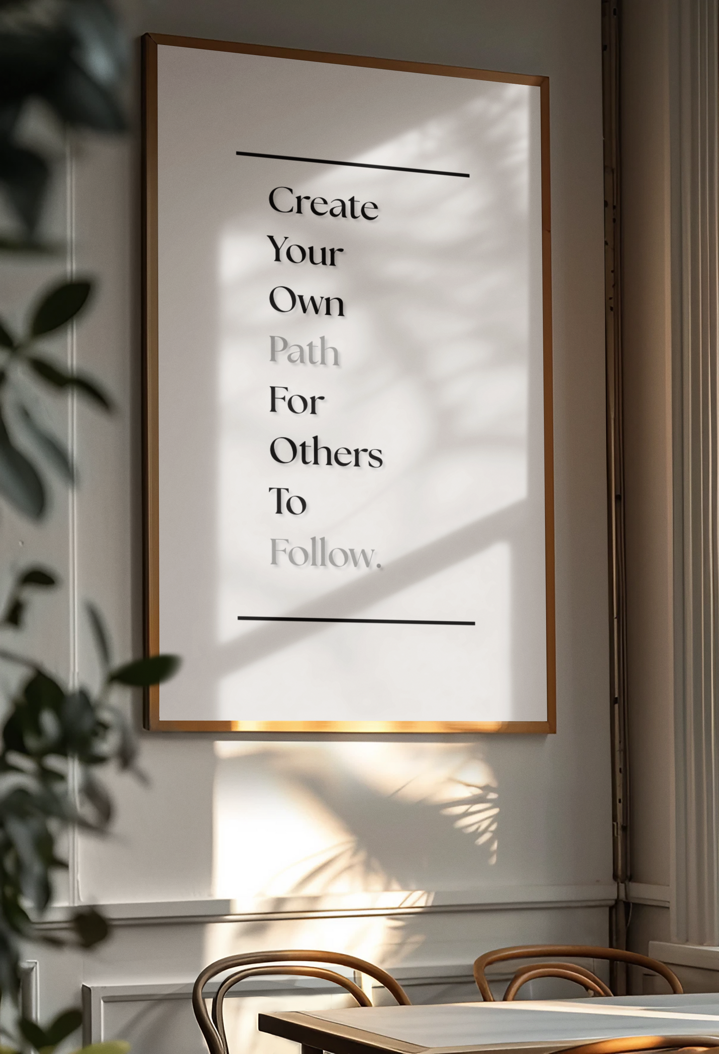 A framed minimalist typographic wall art print hanging on a light gray wall in a dining area. The print features black text reading 'Create Your Own Path For Others To Follow.
