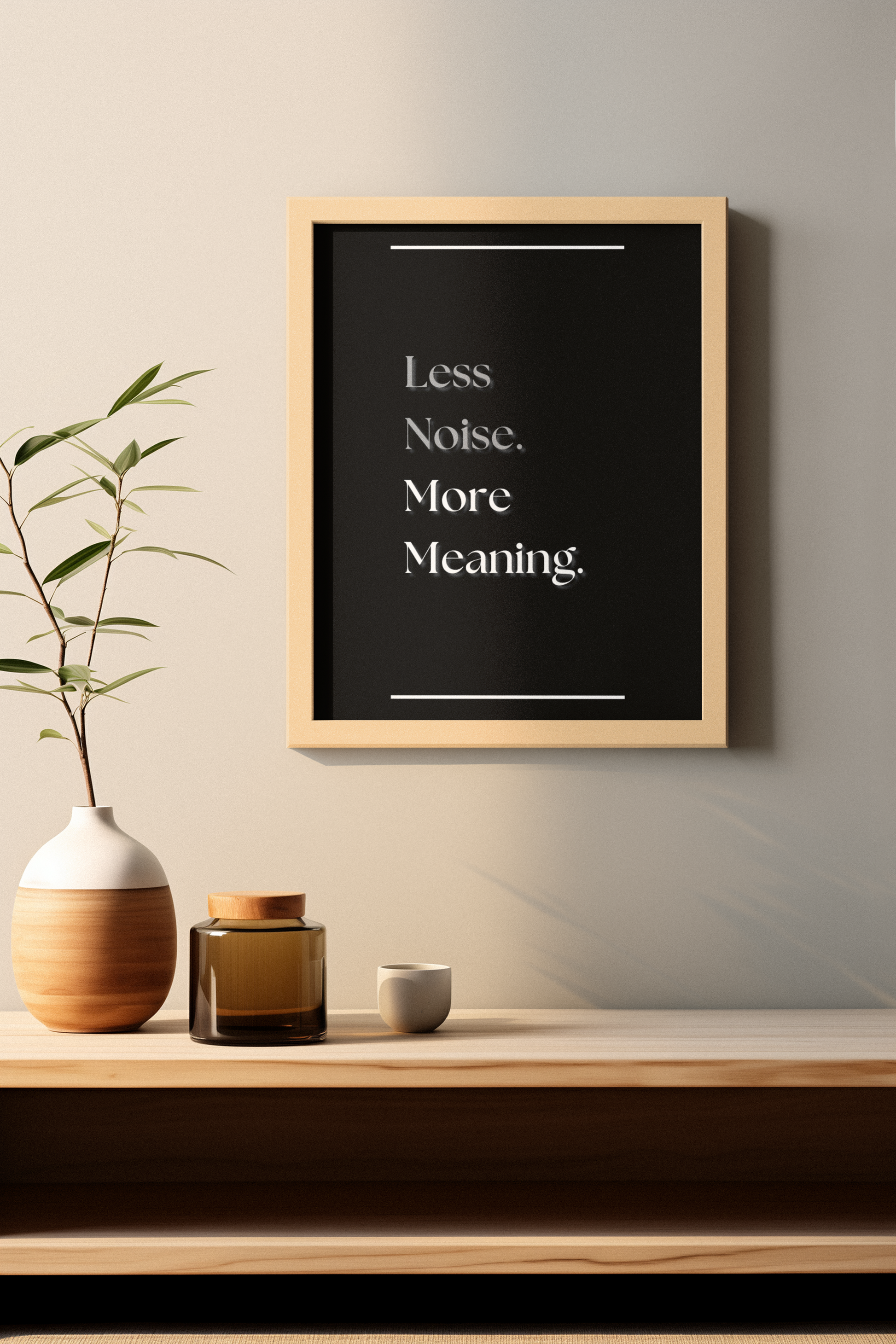 A framed typographic wall art print hangs on a light beige wall above a wooden shelf. The print has a black background with white text reading 'Less Noise. More Meaning'.