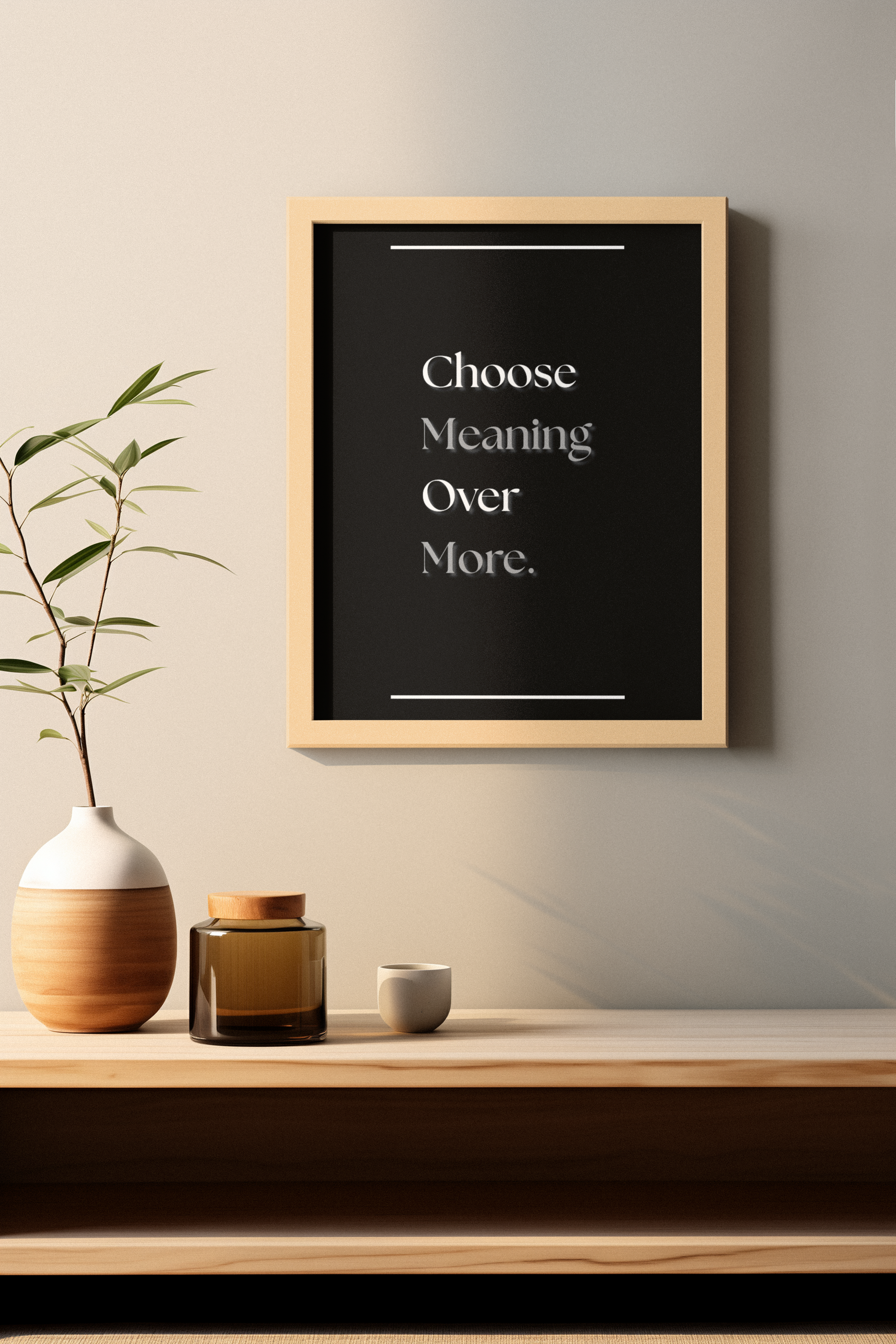 A framed wall art print with the text 'Choose Meaning Over More.' in white serif lettering on a black background, hanging above a wooden shelf with decorative vases and a small cup in a minimalist interior setting.