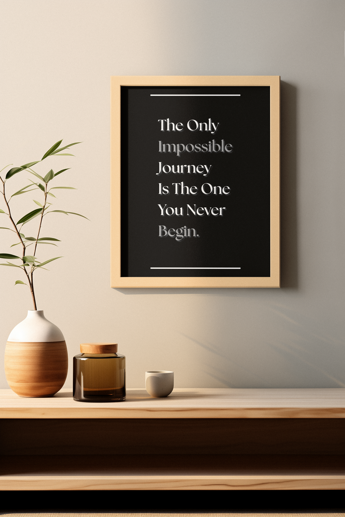 A framed typographic wall art print hangs on a beige wall above a wooden shelf. The print has a black background with white text reading, 'The Only Impossible Journey Is The One You Never Begin.'