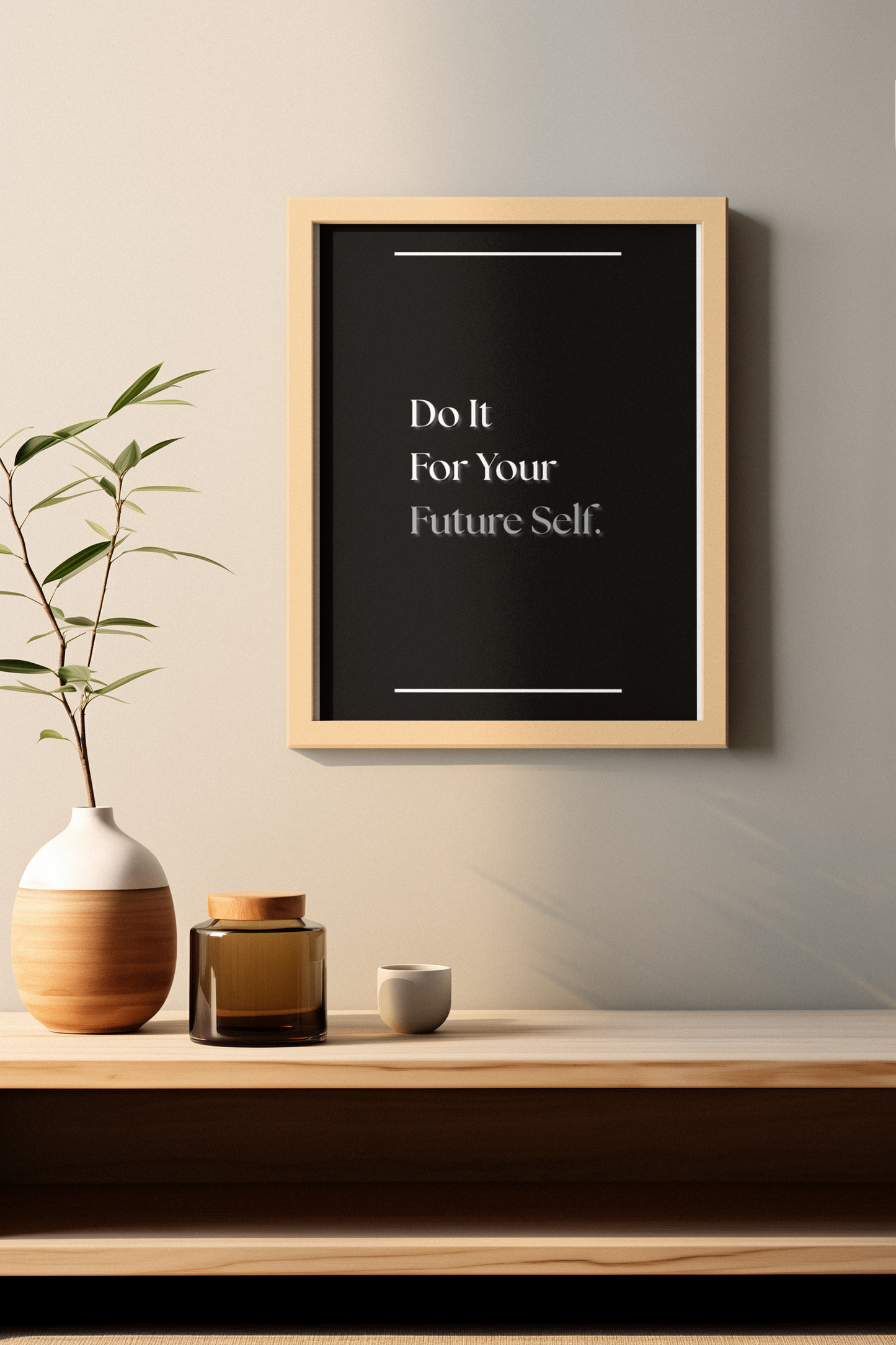 A framed motivational poster with the text 'Do It For Your Future Self.' in white serif text on a black background, hanging on a light beige wall above a wooden shelf with a vase, jar, and small cup.