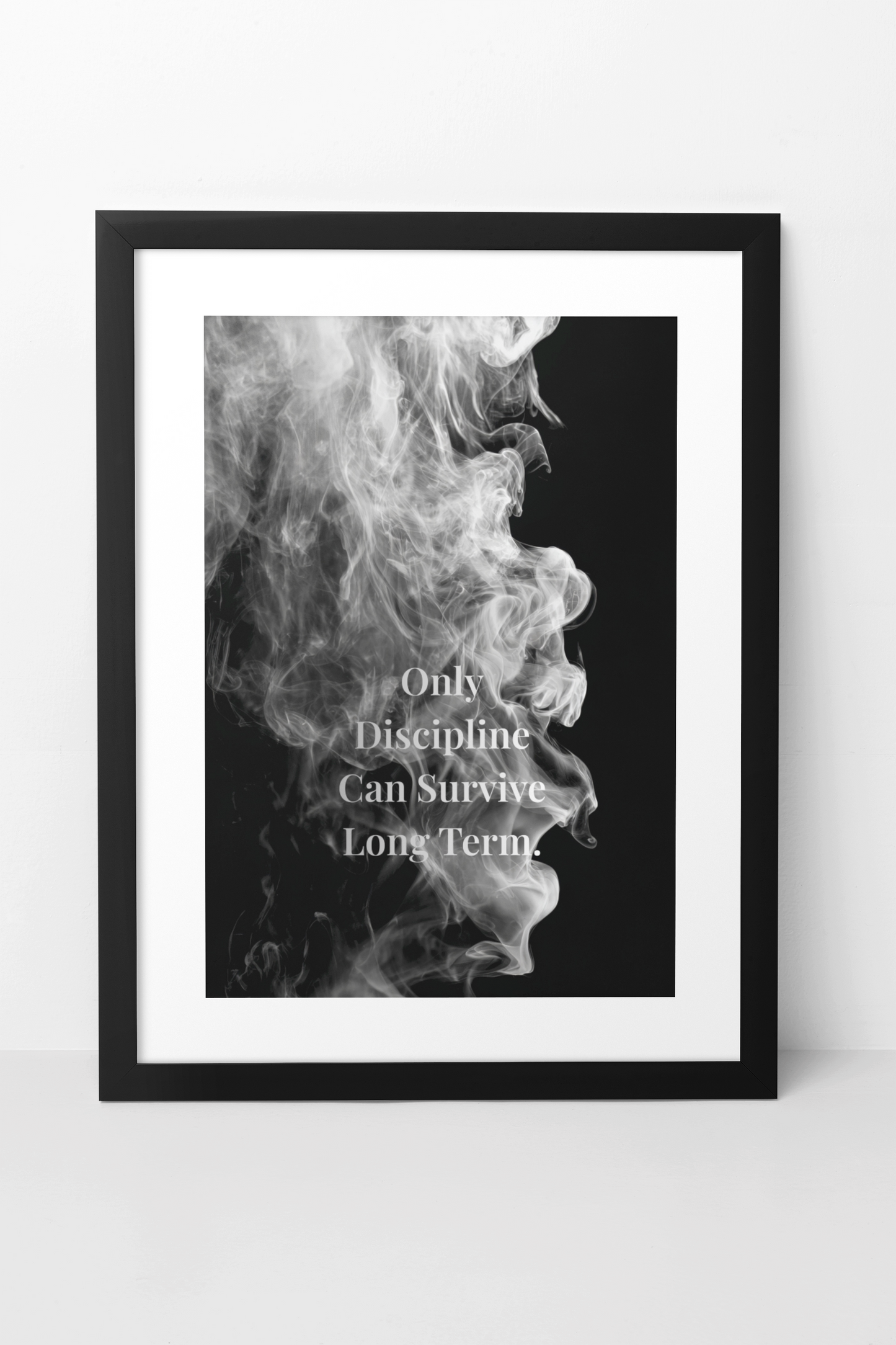 A framed black and white art print featuring a profile of smoke against a black background with the quote 'Only Discipline Can Survive Long Term' in white text, shown in a black frame on a light gray wall.