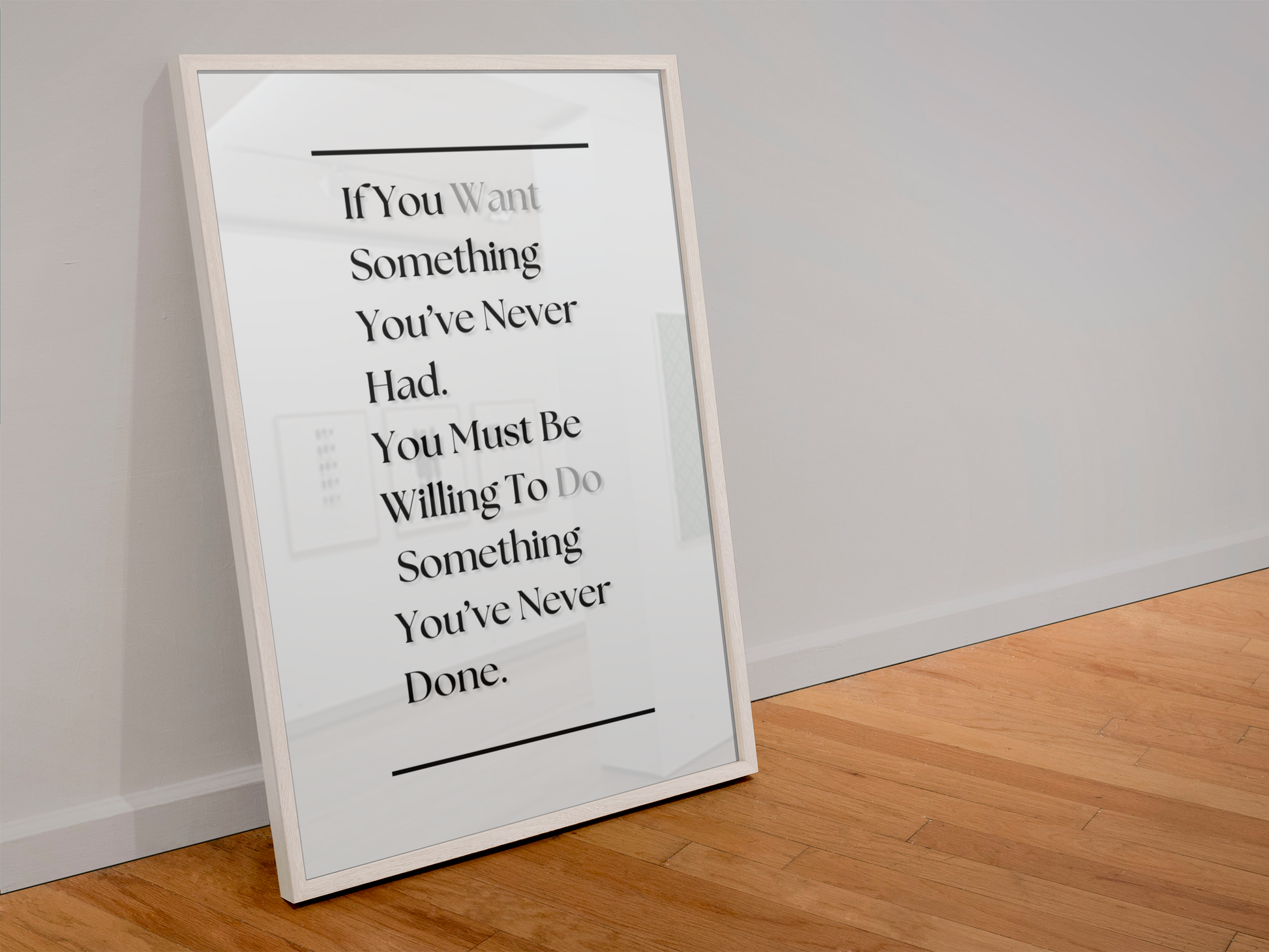A framed motivational quote print leaning against a white wall on a light wood floor. The print features black serif text on a white background with a thin white frame.