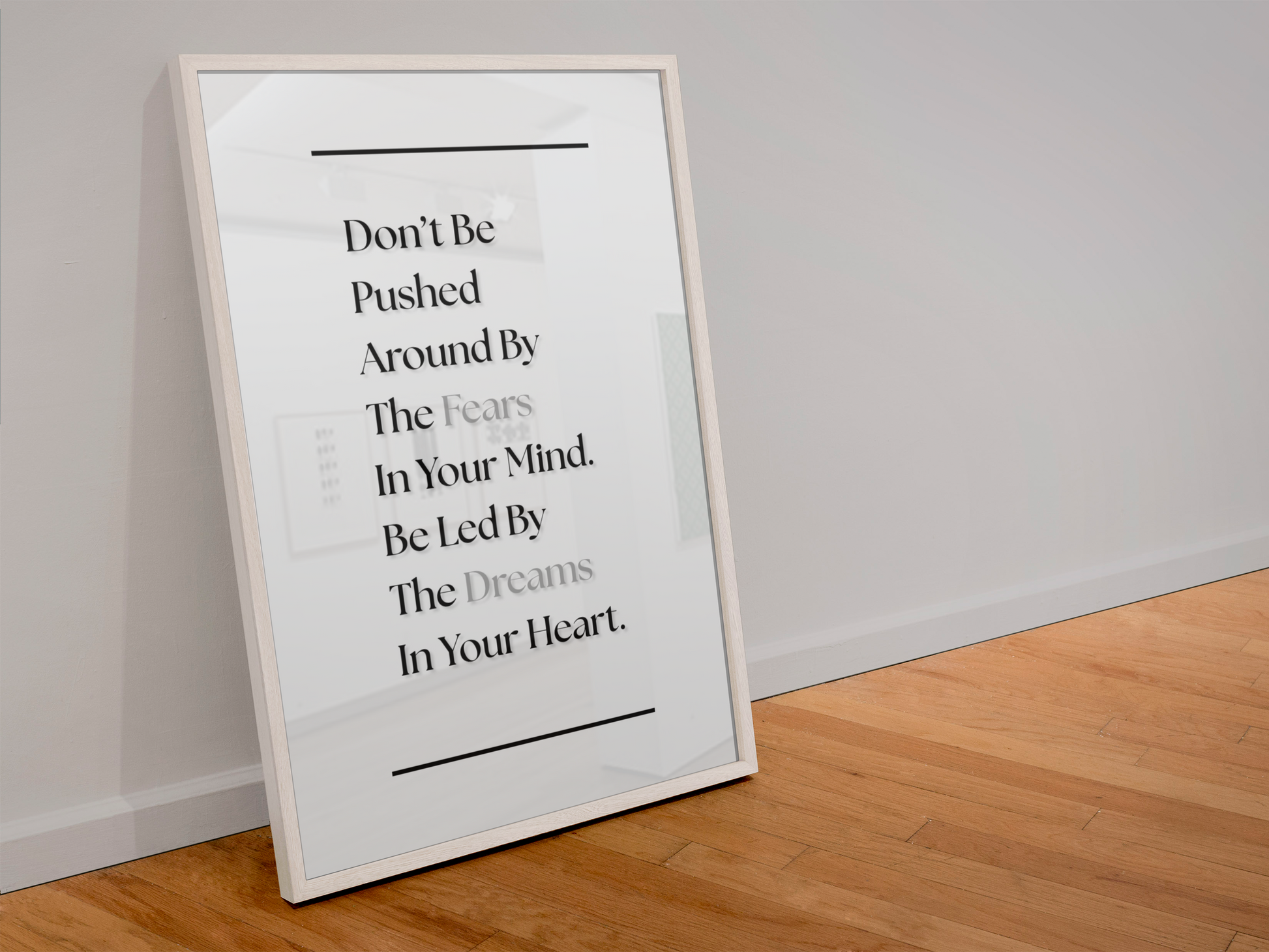 A framed motivational wall art print leaning against a white wall on a light wood floor. The print features a black text quote on a white background with a thin white frame.