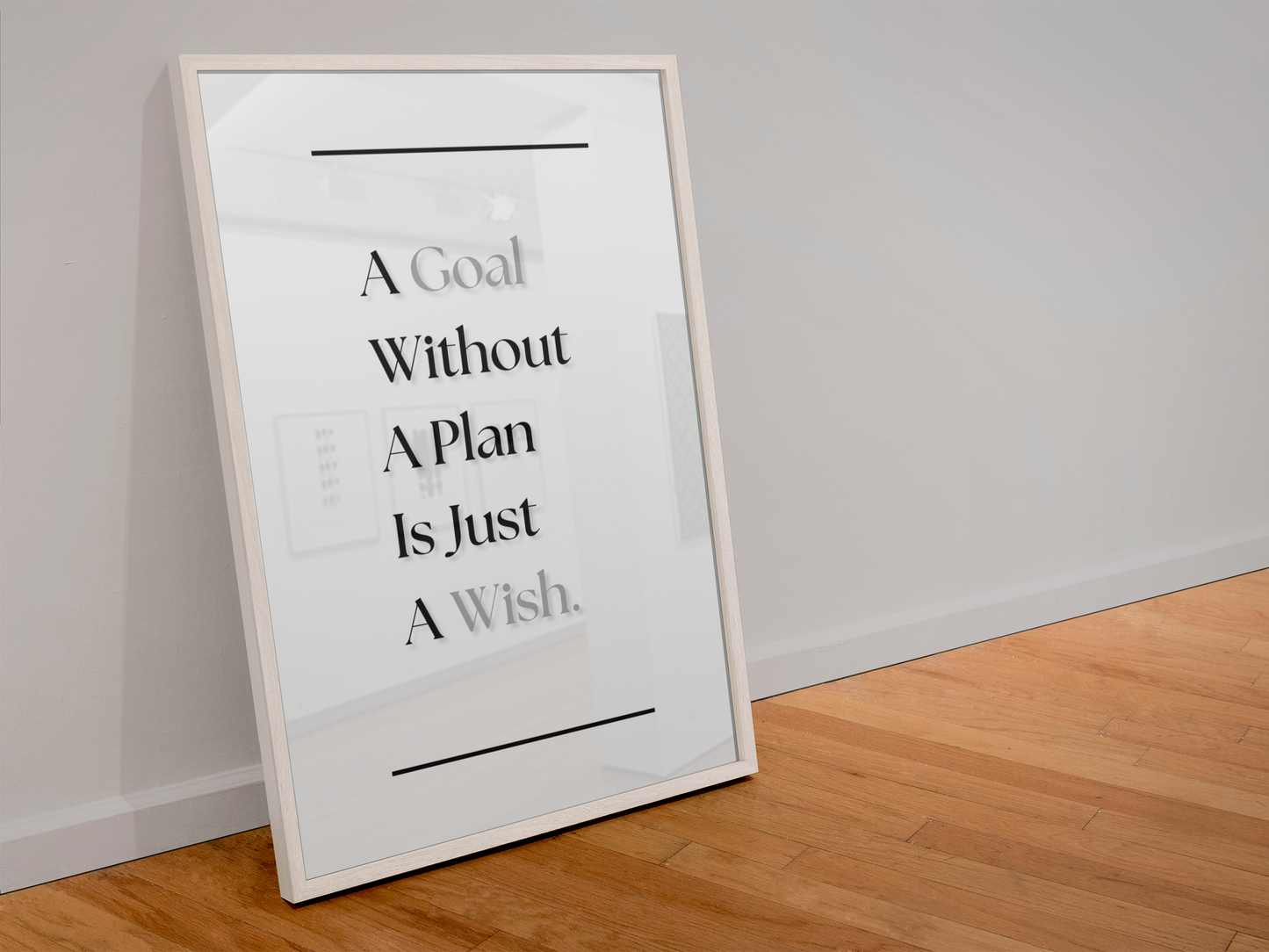 A framed typographic wall art print leaning against a light gray wall on a wood floor. The print reads, 'A Goal Without A Plan Is Just A Wish'.