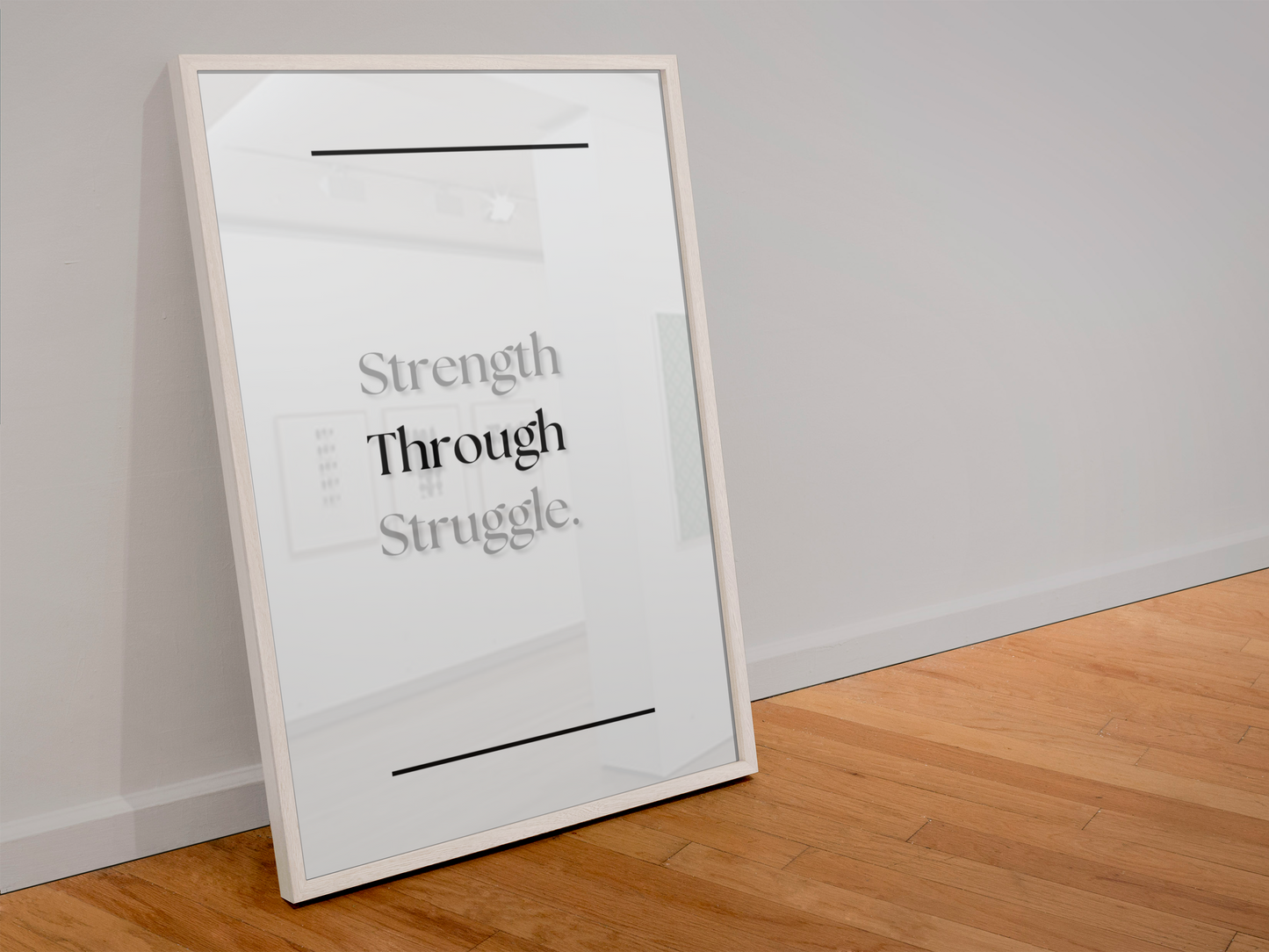 A framed minimalist art print with the text 'Strength Through Struggle.' leaning against a light gray wall on a wooden floor.