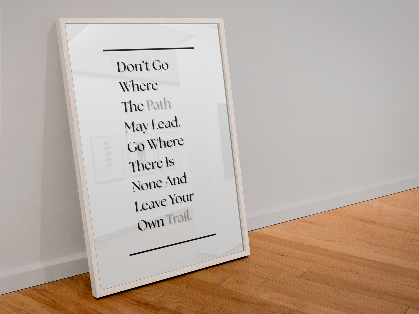 A framed typographic wall art print leaning against a white wall on a light wood floor. The print features a motivational quote in black serif text on a white background with a thin white frame.