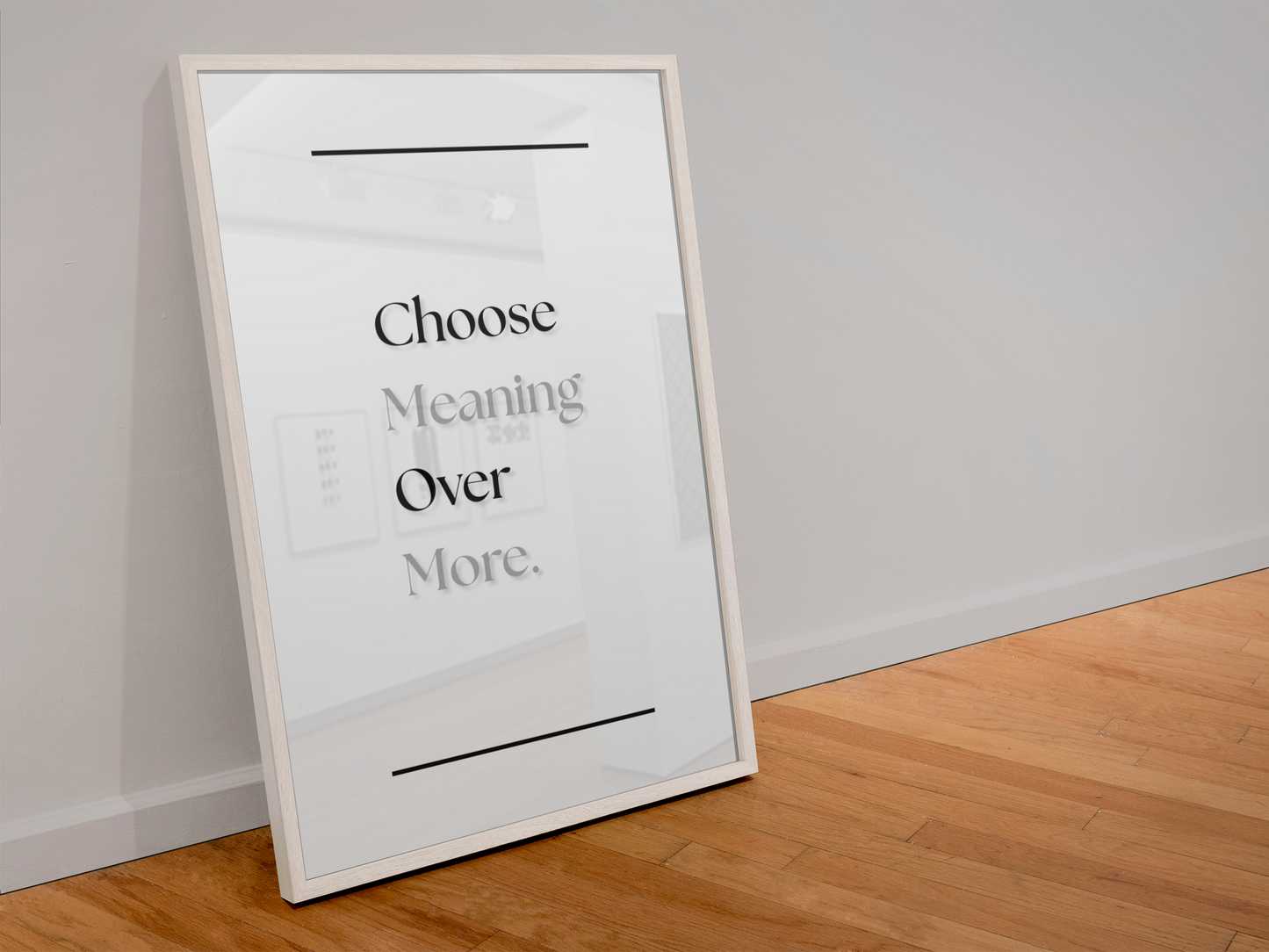 A framed typographic wall art print leaning against a light gray wall on a wood floor. The print has a white background with black text reading 'Choose Meaning Over More.'