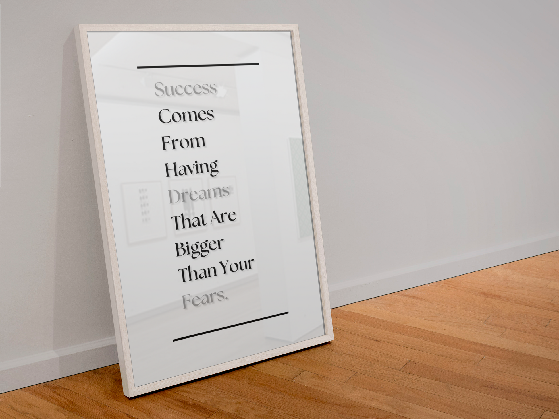A framed motivational art print leaning against a white wall on a light wood floor. The print features a quote about success and dreams in black and gray text on a white background, enclosed in a thin white frame.