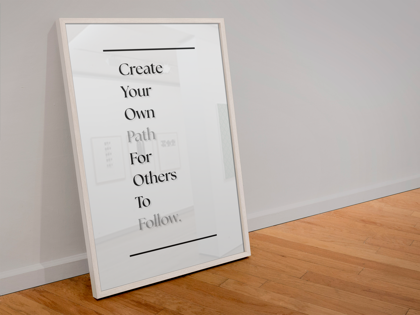 A framed typographic wall art print leaning against a white wall on a light wood floor. The print has a white background with black text reading 'Create Your Own Path For Others To Follow.