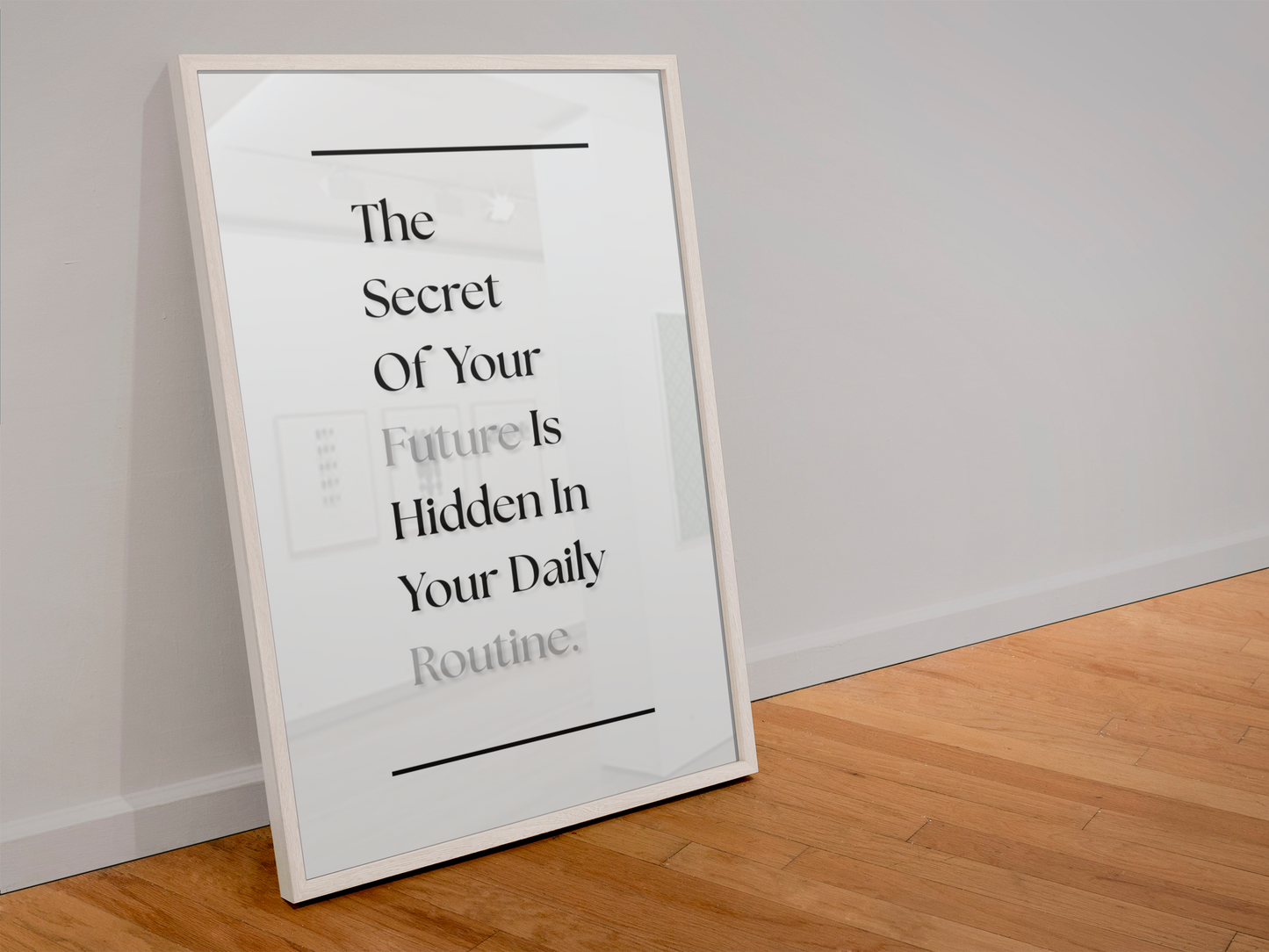 A framed typographic wall art print leaning against a white wall on a light wood floor. The print has a white background with black text reading, 'The Secret Of Your Future Is Hidden In Your Daily Routine'.