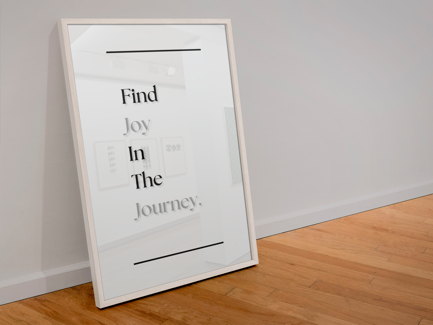 A framed minimalist art print leaning against a white wall on a light wood floor. The print features the text 'Find Joy In The Journey.