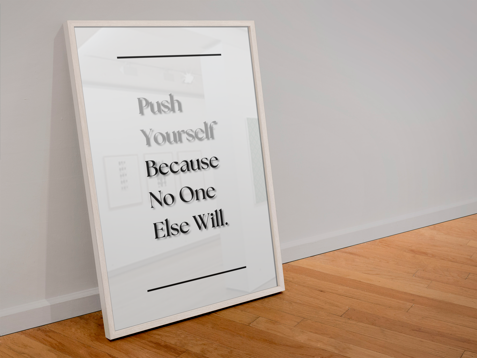 A framed motivational quote print leaning against a white wall on a light wood floor. The print features black serif text reading 'Push Yourself Because No One Else Will'.