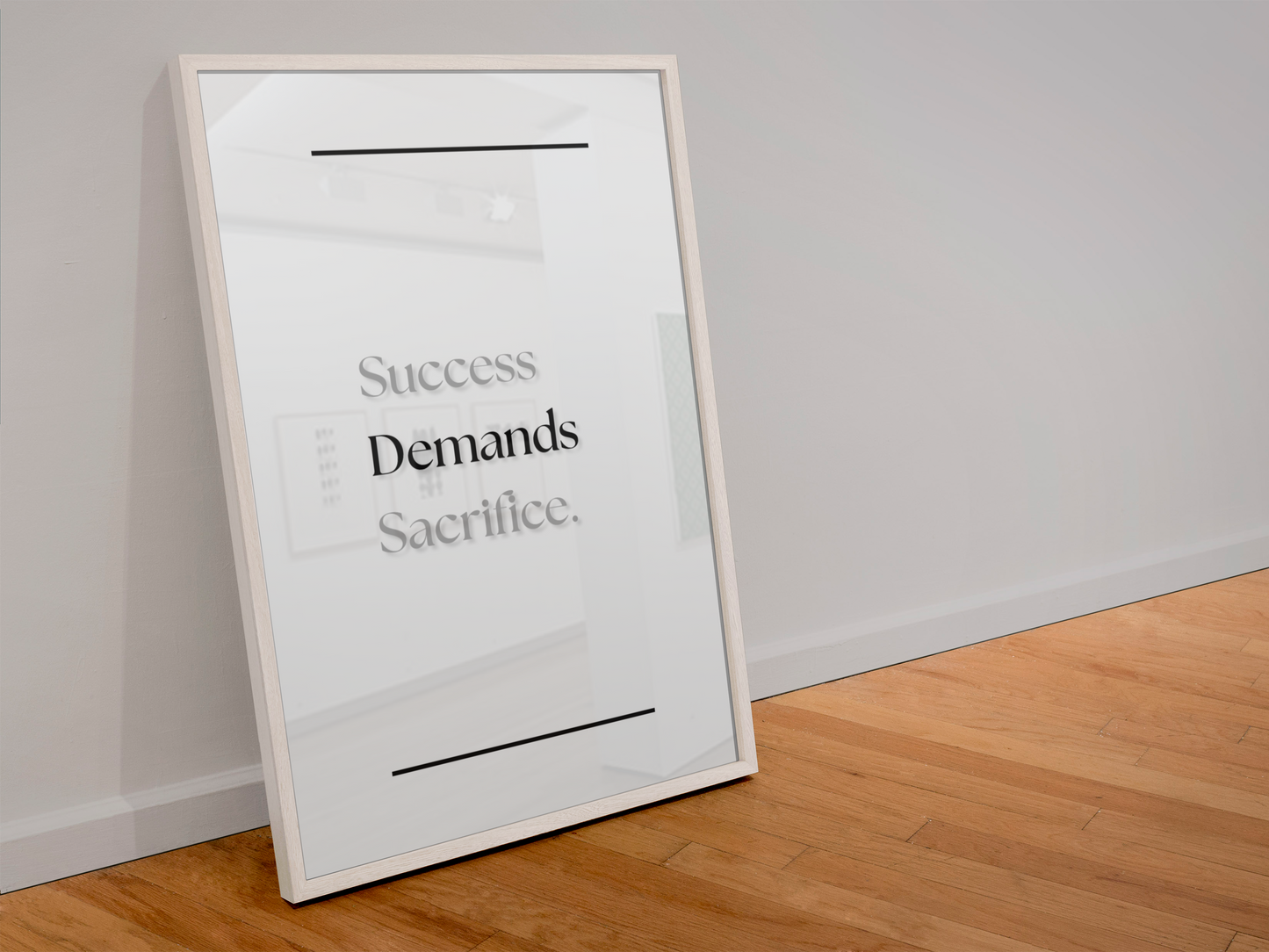 A framed motivational art print leaning against a white wall on a light wood floor. The print features the quote 'Success Demands Sacrifice'.