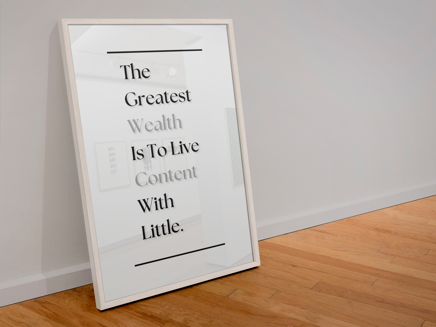 A framed typographic wall art print leaning against a white wall on a light wood floor. The print features black serif text reading, 'The Greatest Wealth Is To Live Content With Little'.