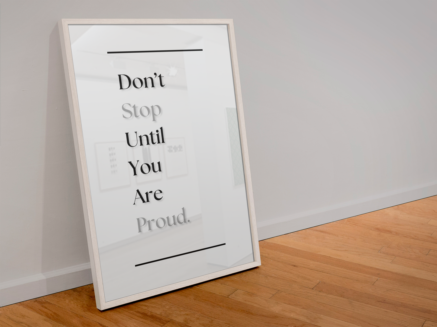 A framed motivational wall art print leaning against a white wall on a light wood floor. The print features the text 'Don't Stop Until You Are Proud' in black and gray lettering on a white background, enclosed in a thin white frame.