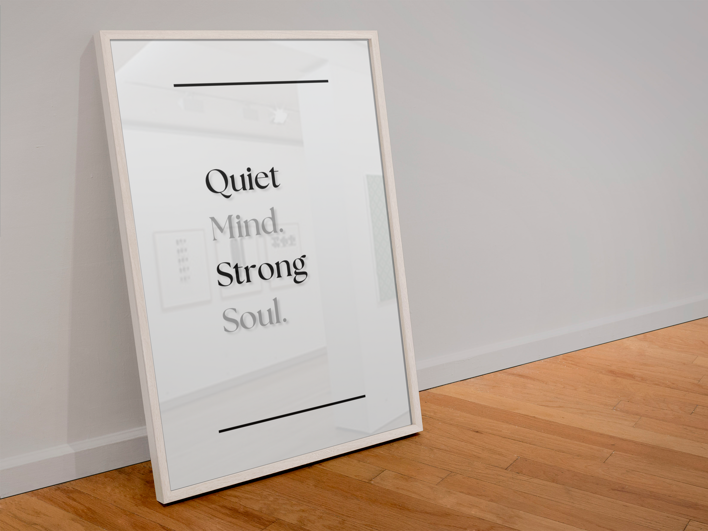 A framed typographic wall art print leaning against a light gray wall on a wood floor. The print has a white background with black text reading 'Quiet Mind Strong Soul.'